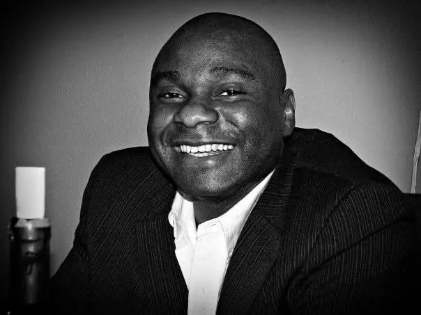 Osato Eugene Uzamere a NYC attorney, smiling man in a suit sitting indoors with a plain background