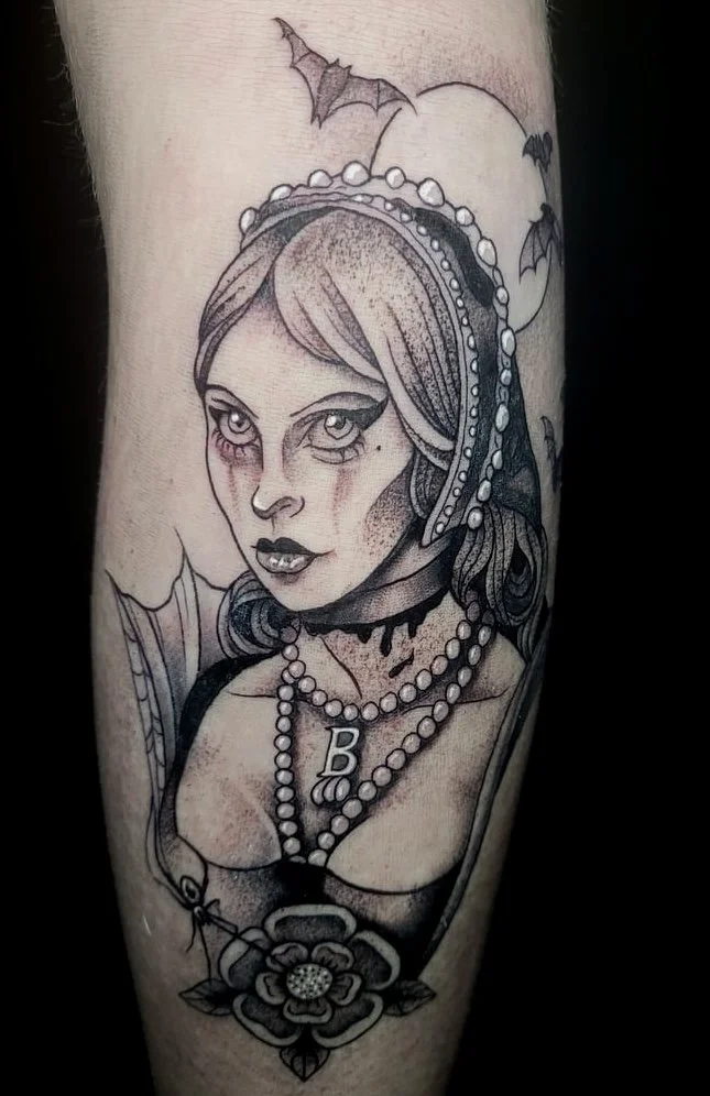 Tattoo of a woman with a choker necklace and pearl necklaces, with gothic makeup, and dark hair with curls, surrounded by bats and a full moon in the background.