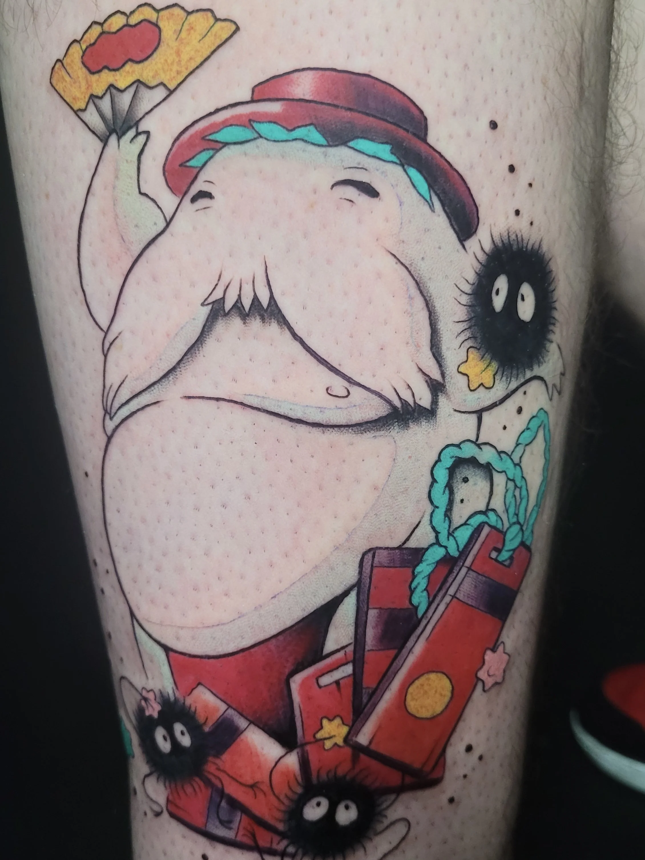 A colorful tattoo of an old man with a big belly, holding a slice of pizza, with cartoonish black fuzzy creatures surrounding him, and some building blocks and ropes at the bottom.
