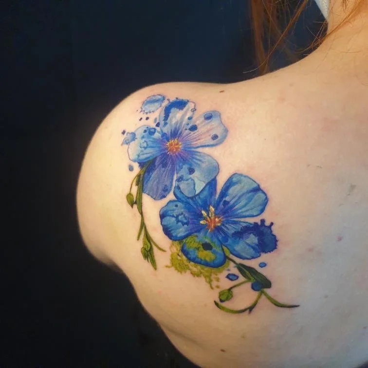 Tattoo of blue flowers on person's shoulder with green stems and yellow accents.
