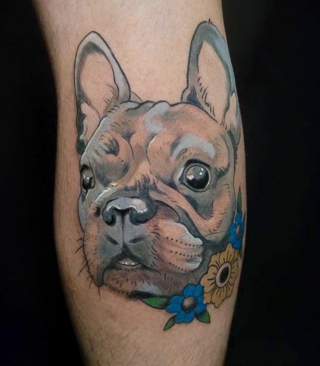 Tattoo of a dog’s face, possibly a French Bulldog or Boston Terrier, surrounded by colorful flowers on the person's arm.
