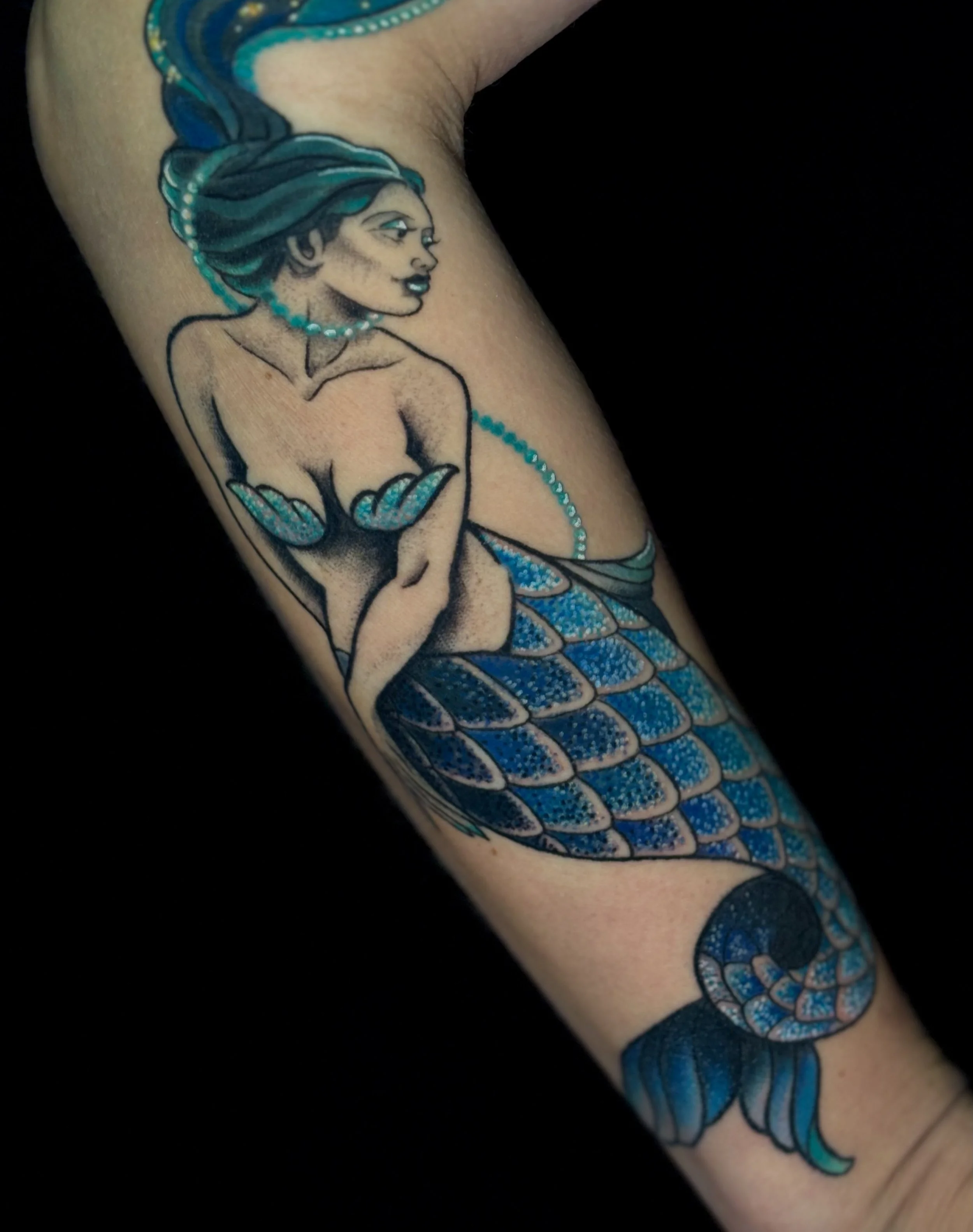 Tattoo of a mermaid with blue hair and tail on person's arm.