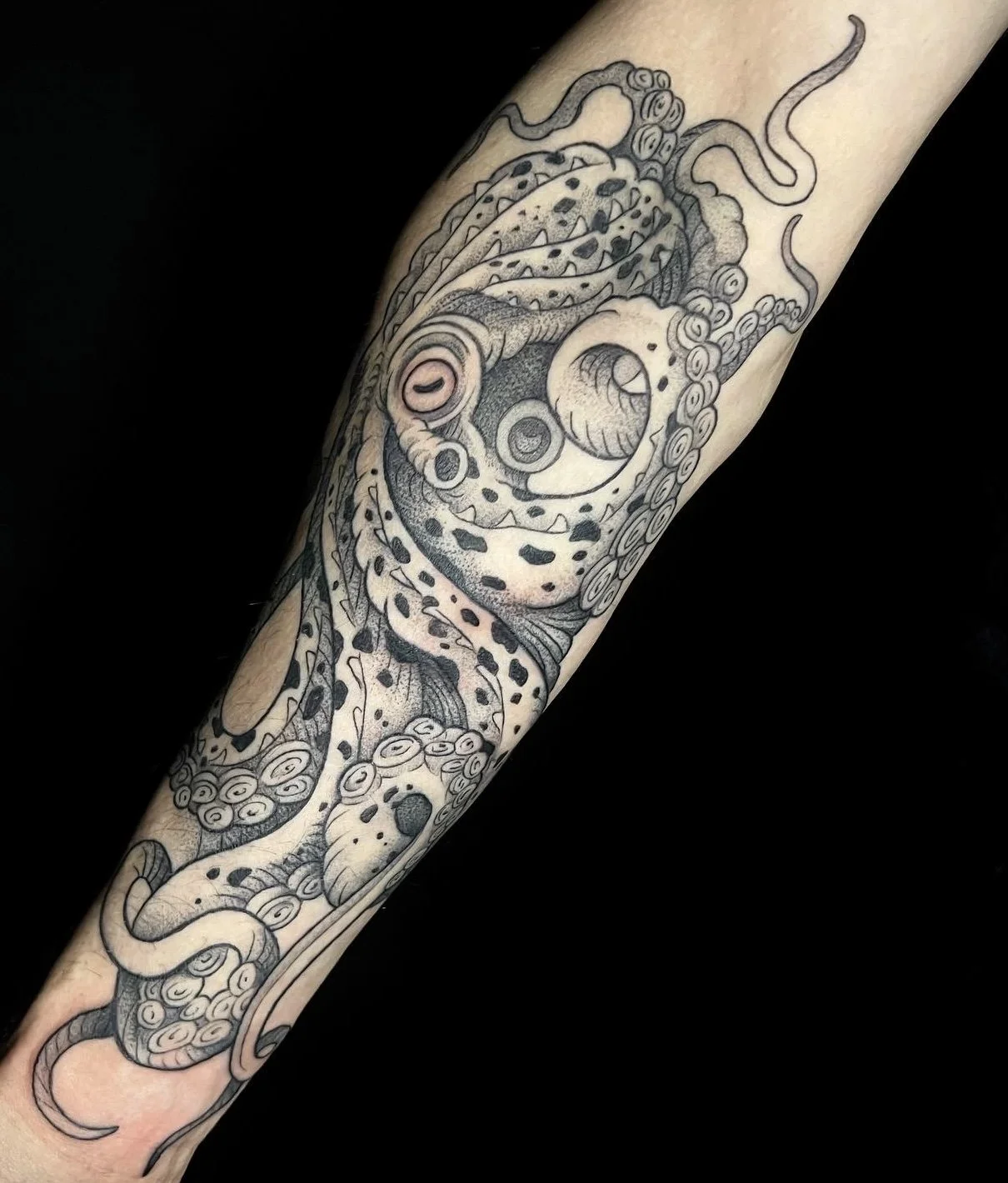 Black and gray tattoo of an octopus on a person's arm, with tentacles curling and detailed shading.