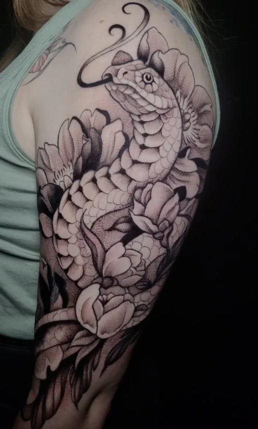 A black and gray tattoo of a snake intertwined with peony flowers on a person's upper arm and shoulder.