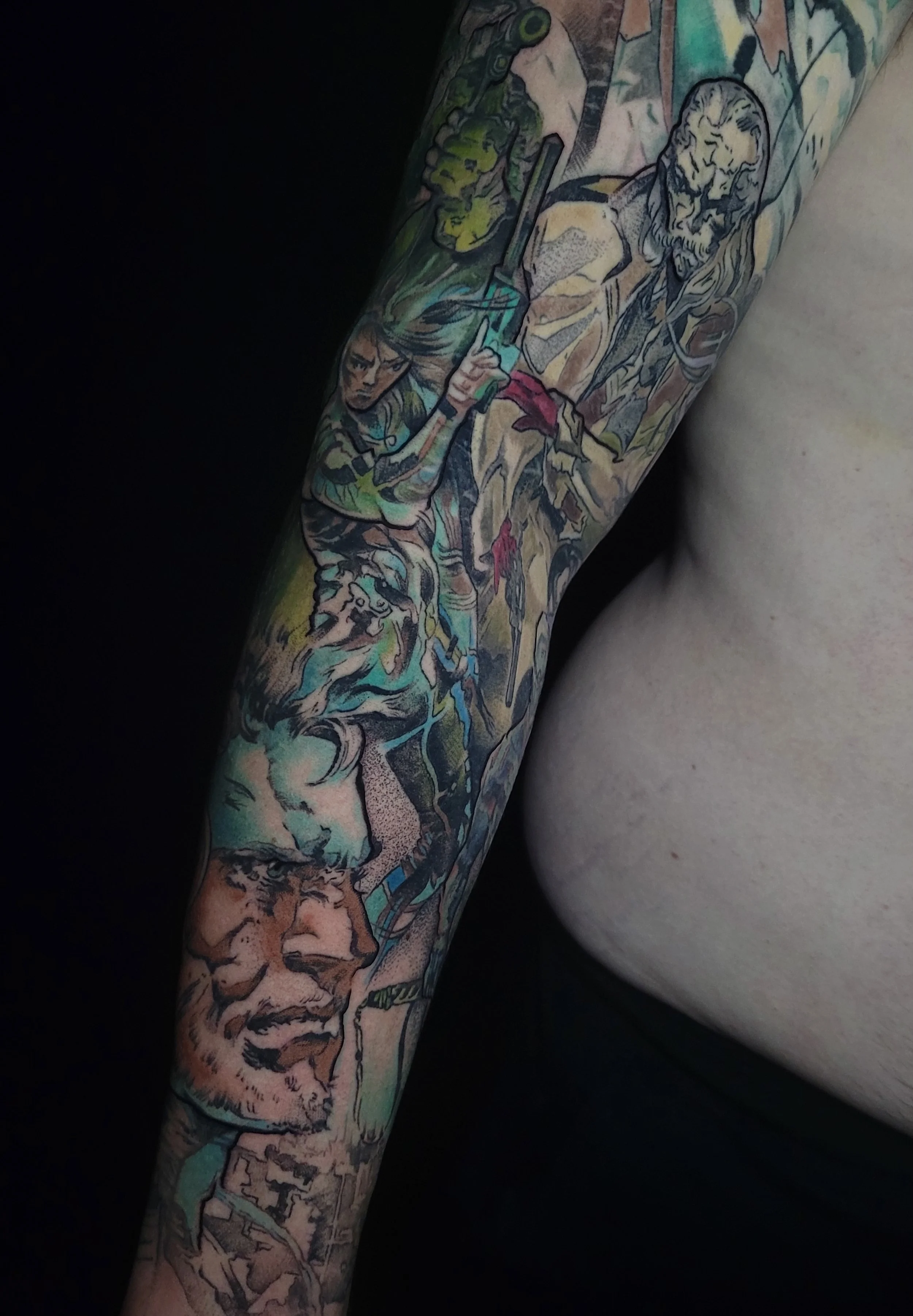 Close-up of a colorful tattoo sleeve featuring various characters, including a man with long hair and a beard, a woman with a bow, a lion, and other detailed elements.