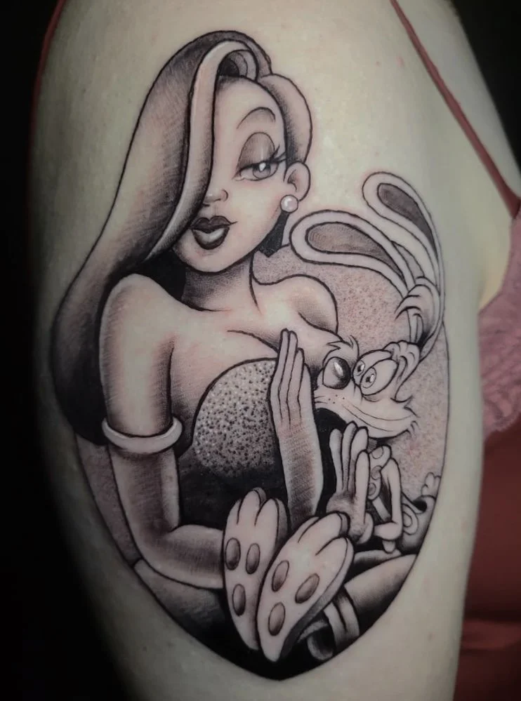 A black and gray tattoo featuring a stylized cartoon woman with wavy hair, wearing a pearl earring and a strapless dress, winking and smiling. She is holding a cartoon lobster with large eyes and expressive claws in her arms.