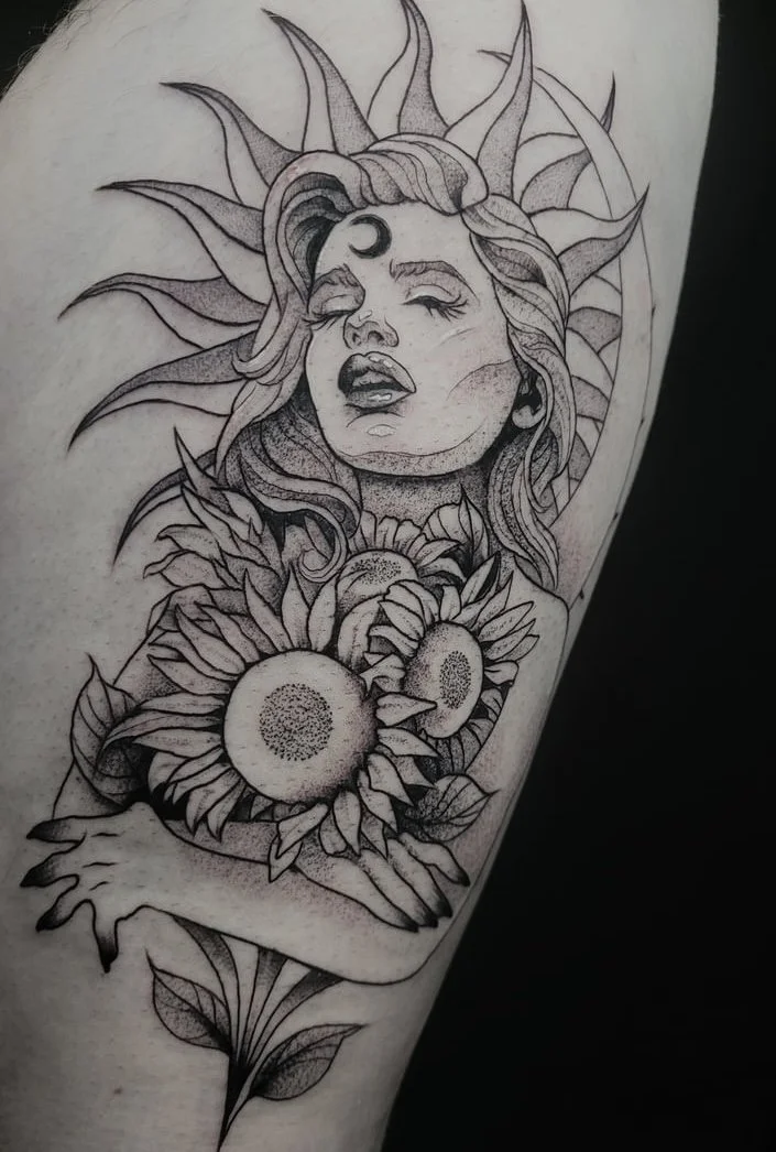 Tattoo of a woman's face with a crescent moon on her forehead, surrounded by sunflowers and sun-shaped rays.