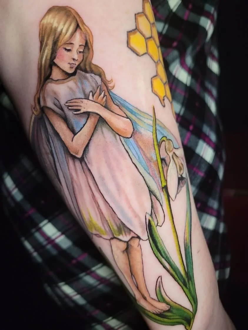 A colorful tattoo of a girl with long hair, wearing a dress, standing with her arms crossed over her chest. The tattoo includes a large yellow honeycomb and a flower along her leg.