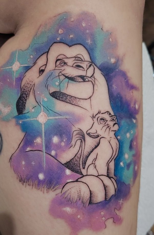 Tattoo of two lions, one larger and smiling, and a smaller lion cub, with a colorful galaxy background.