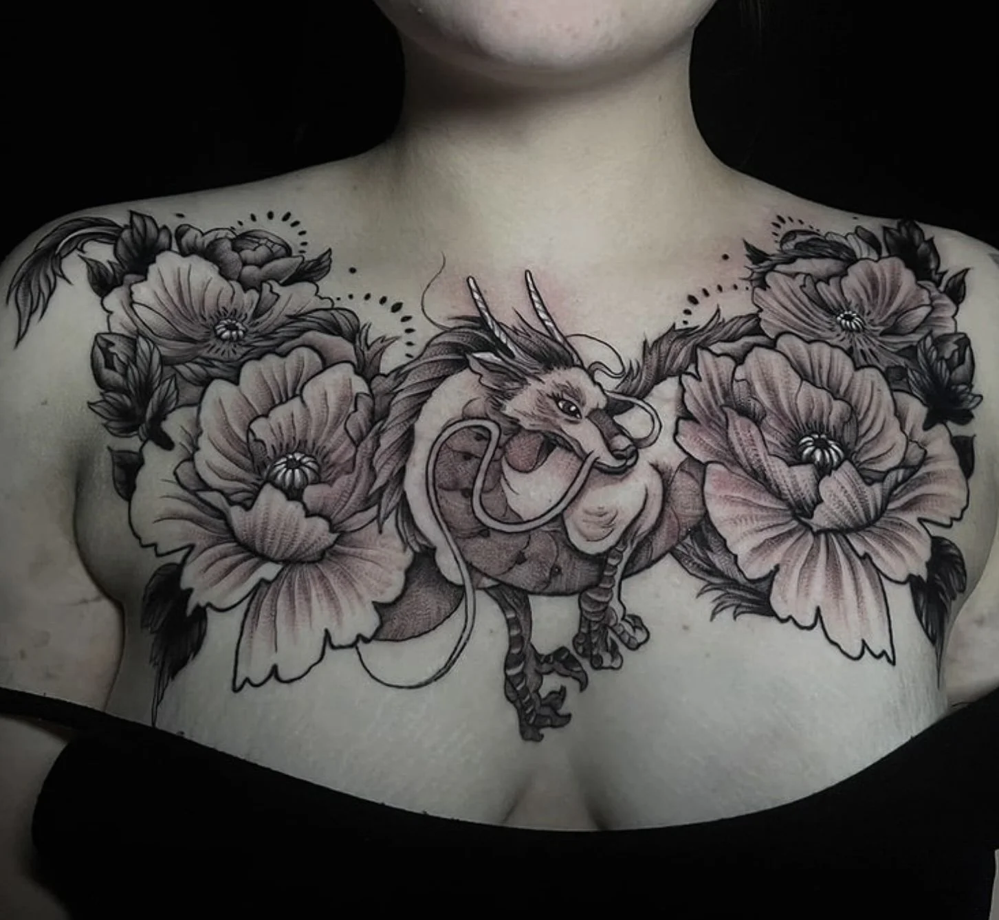 Black and gray chest tattoo featuring a dragon intertwined with large floral elements, including peonies, on a person's chest.