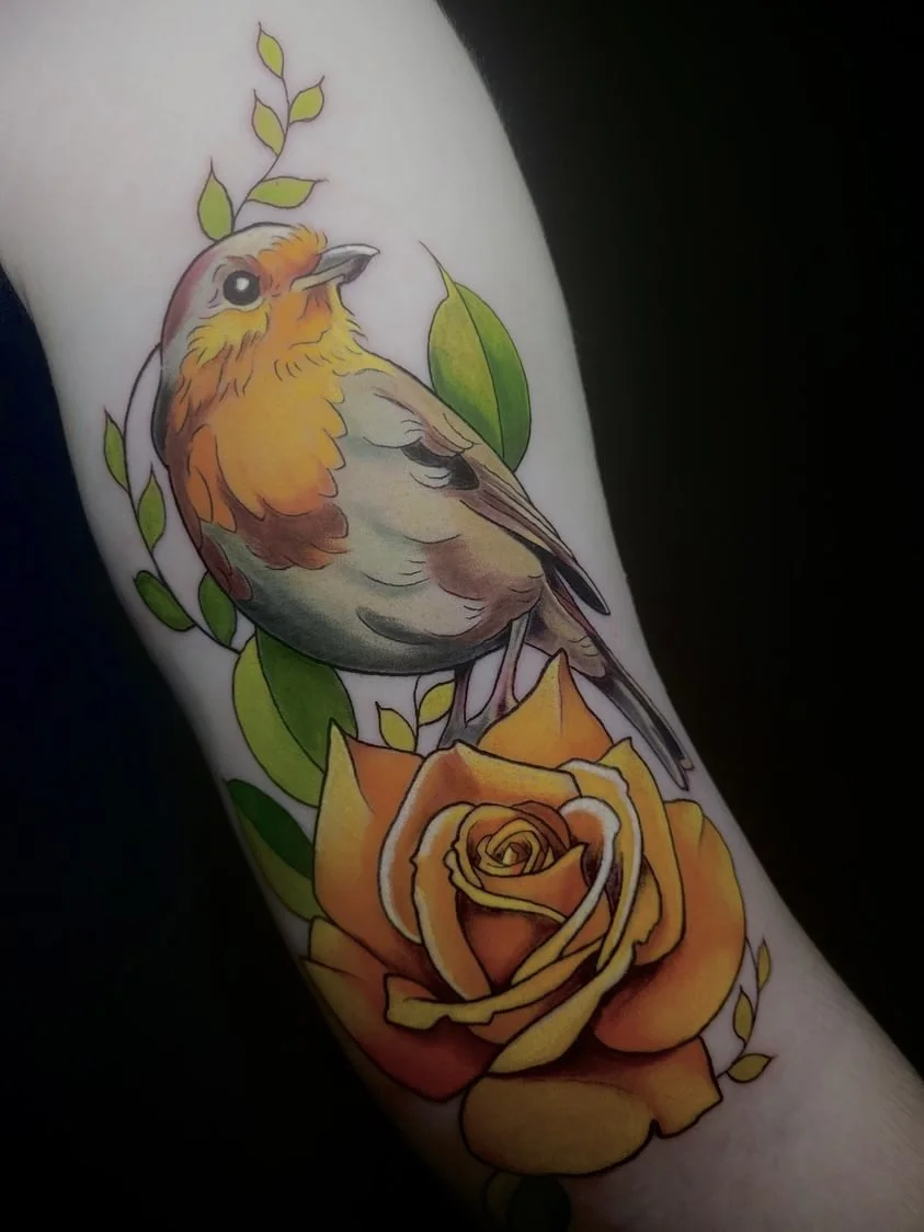 Color tattoo of a bird perched on a yellow rose with green leaves.