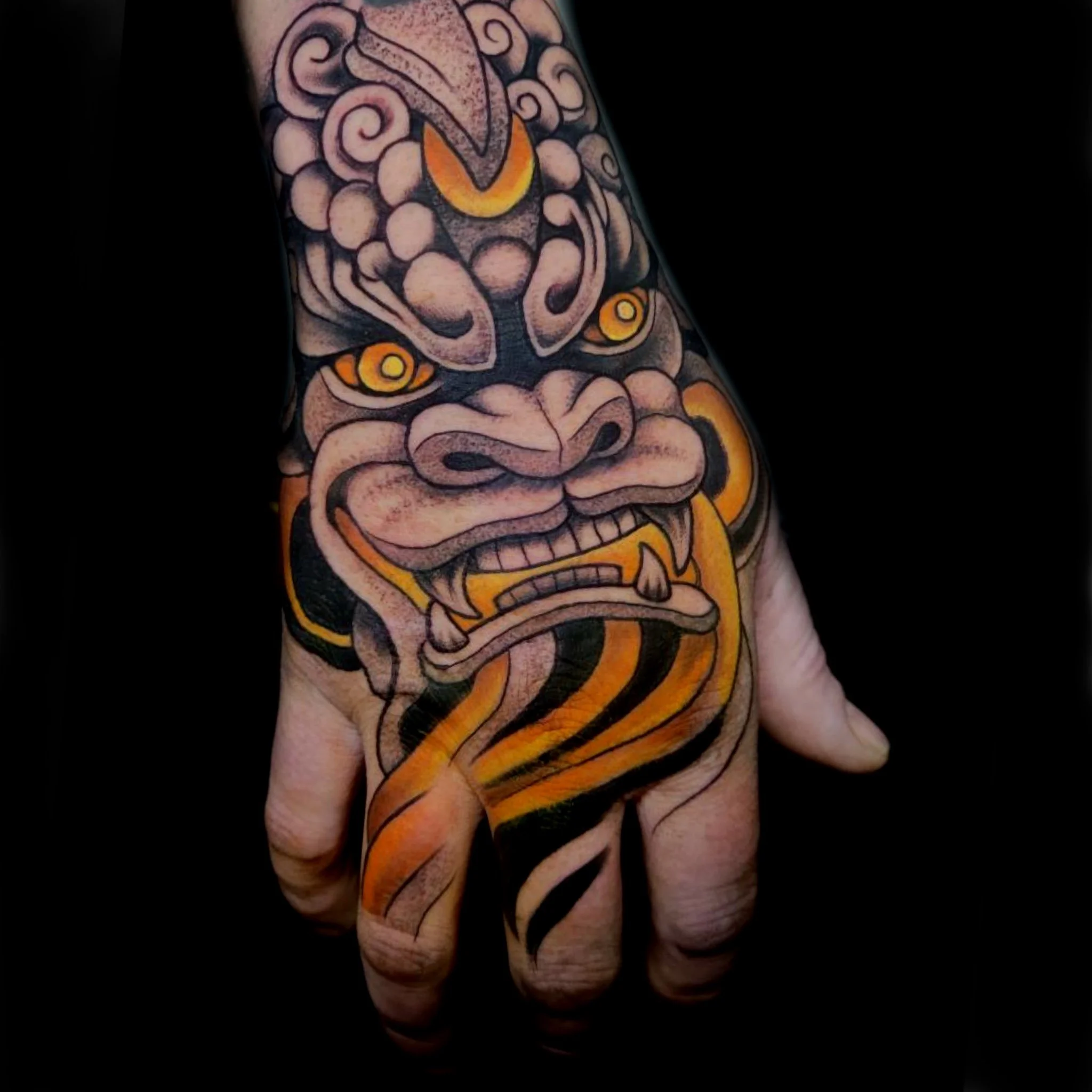 Tattoo of a fierce tiger face on hand and forearm with black, orange, and cream colors.