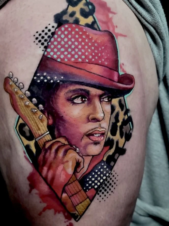 Colorful tattoo of a woman with a cowboy hat holding a guitar, surrounded by leopard print and dotted patterns.