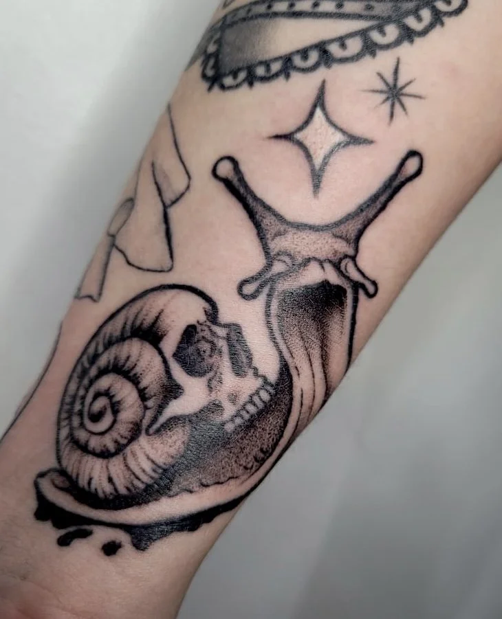 Tattoo of a snail with a skull inside its shell and a small star above, on a person's arm.
