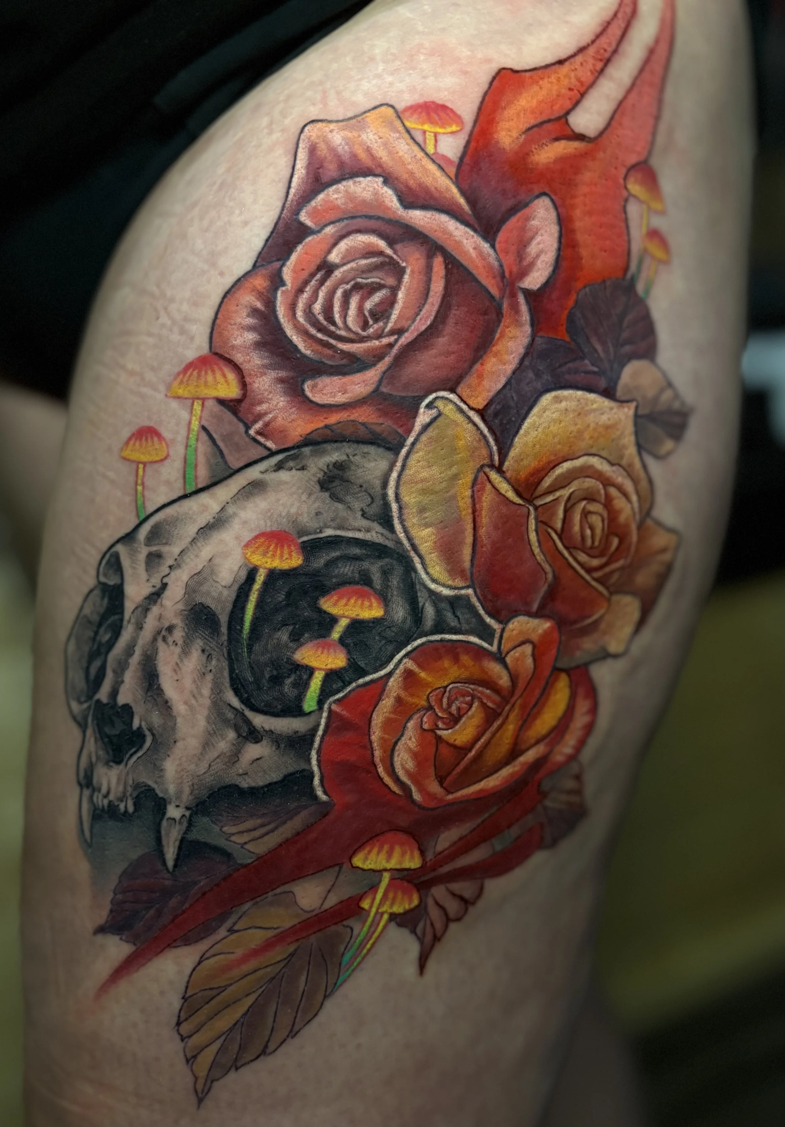 A tattoo featuring a detailed skull adorned with roses, mushrooms, and a dragonfly, rendered in vibrant colors.