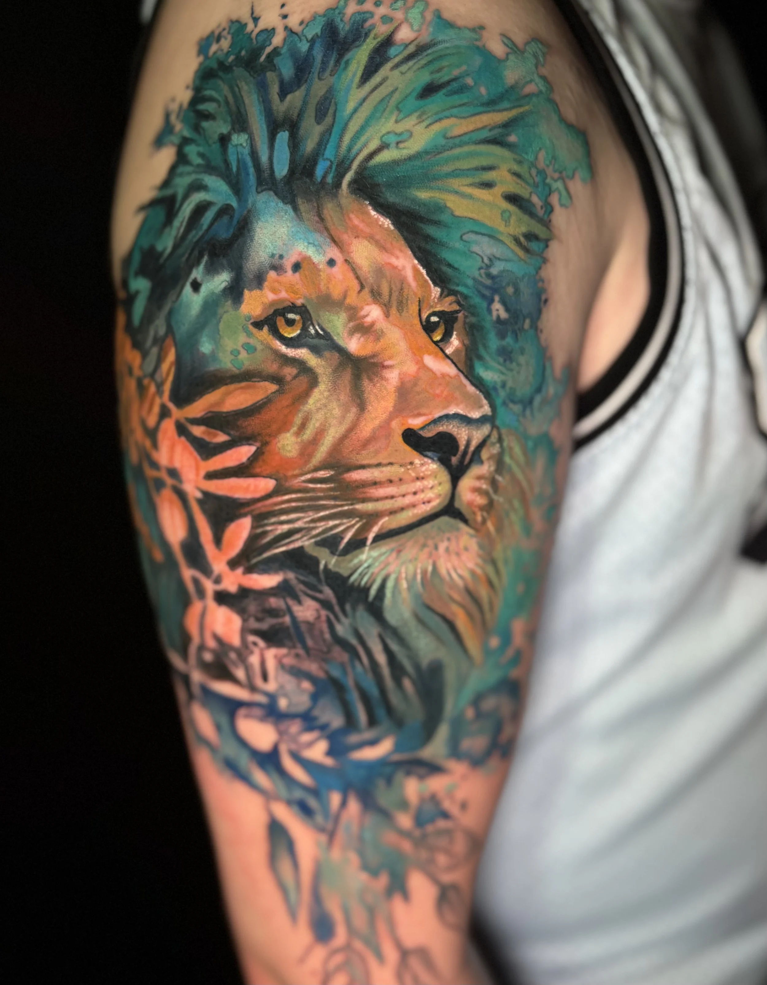 Colorful tattoo of a lion's face with a mane, on a person's upper arm.