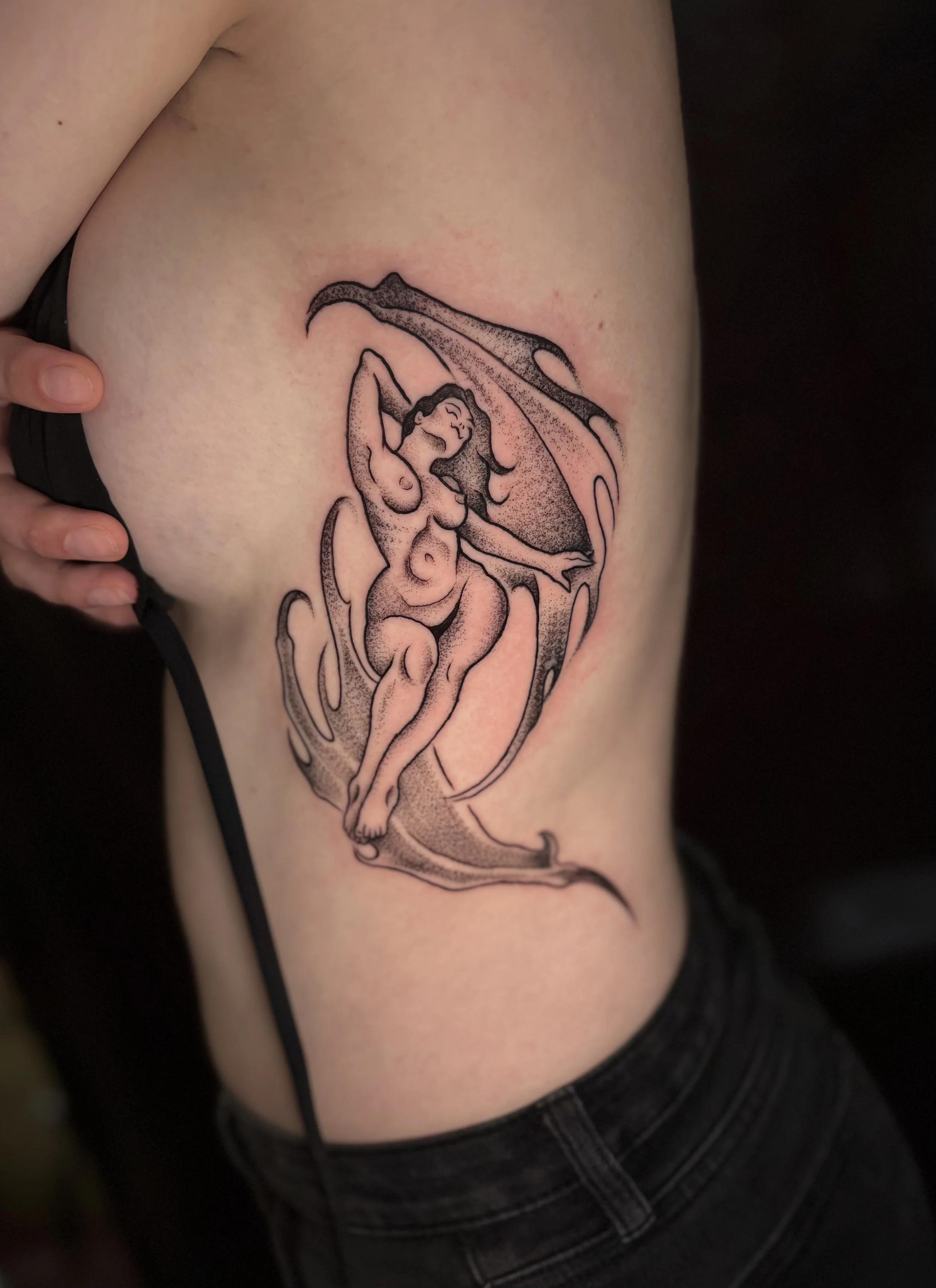 Tattoo of a woman with flowing hair, in a reclining pose, surrounded by abstract waves or flames.