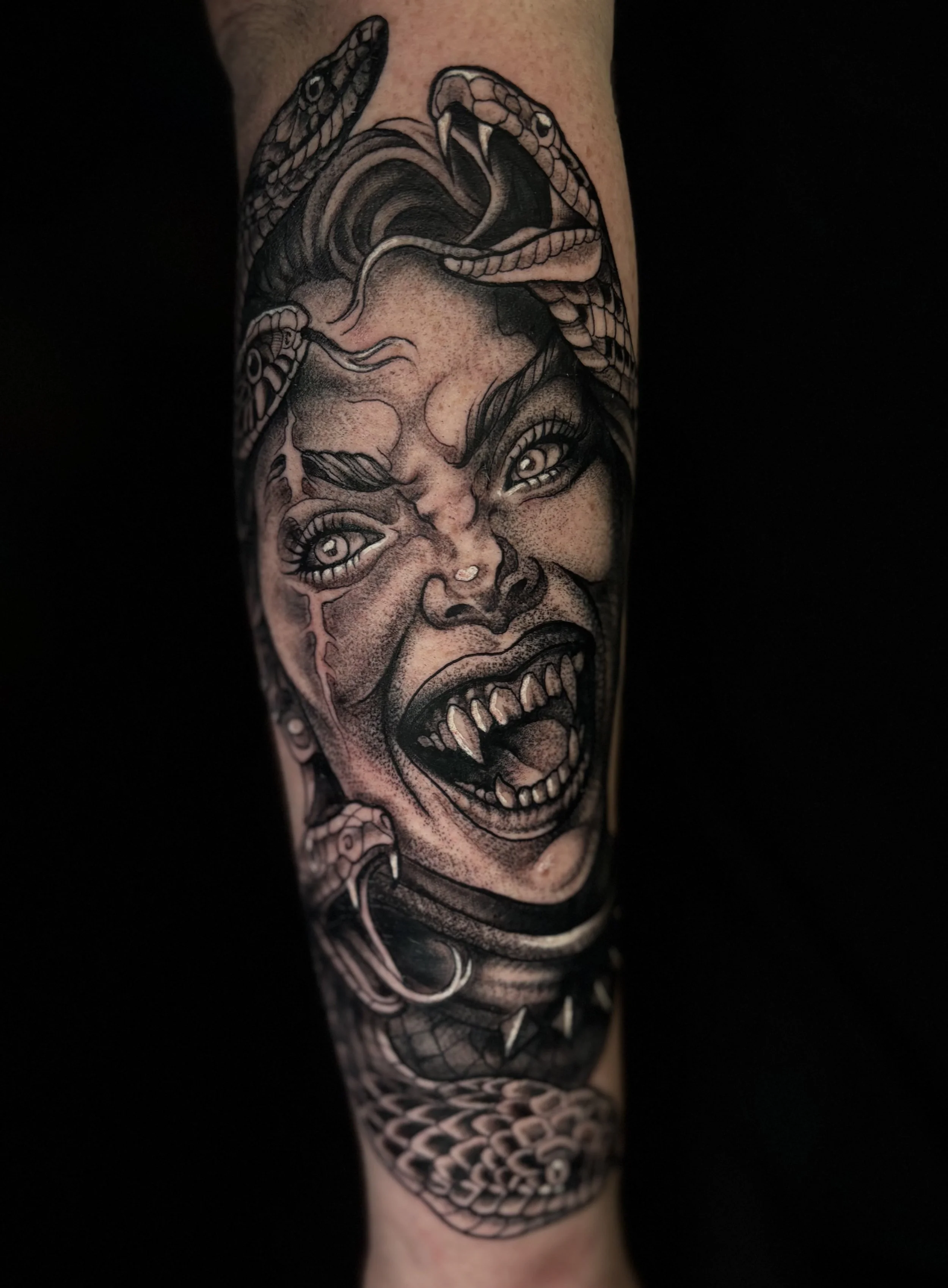 Black and gray tattoo of a snarling woman with snake-like features.