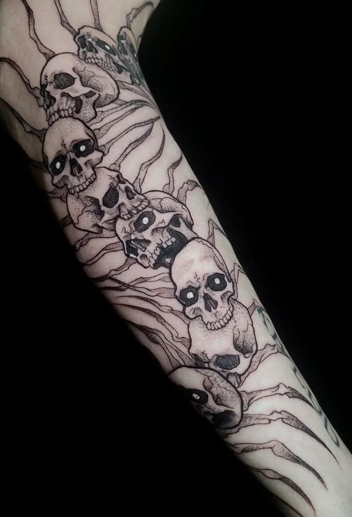 Tattoo of multiple skulls with hollow eyes arranged vertically along the arm, with detailed line work.