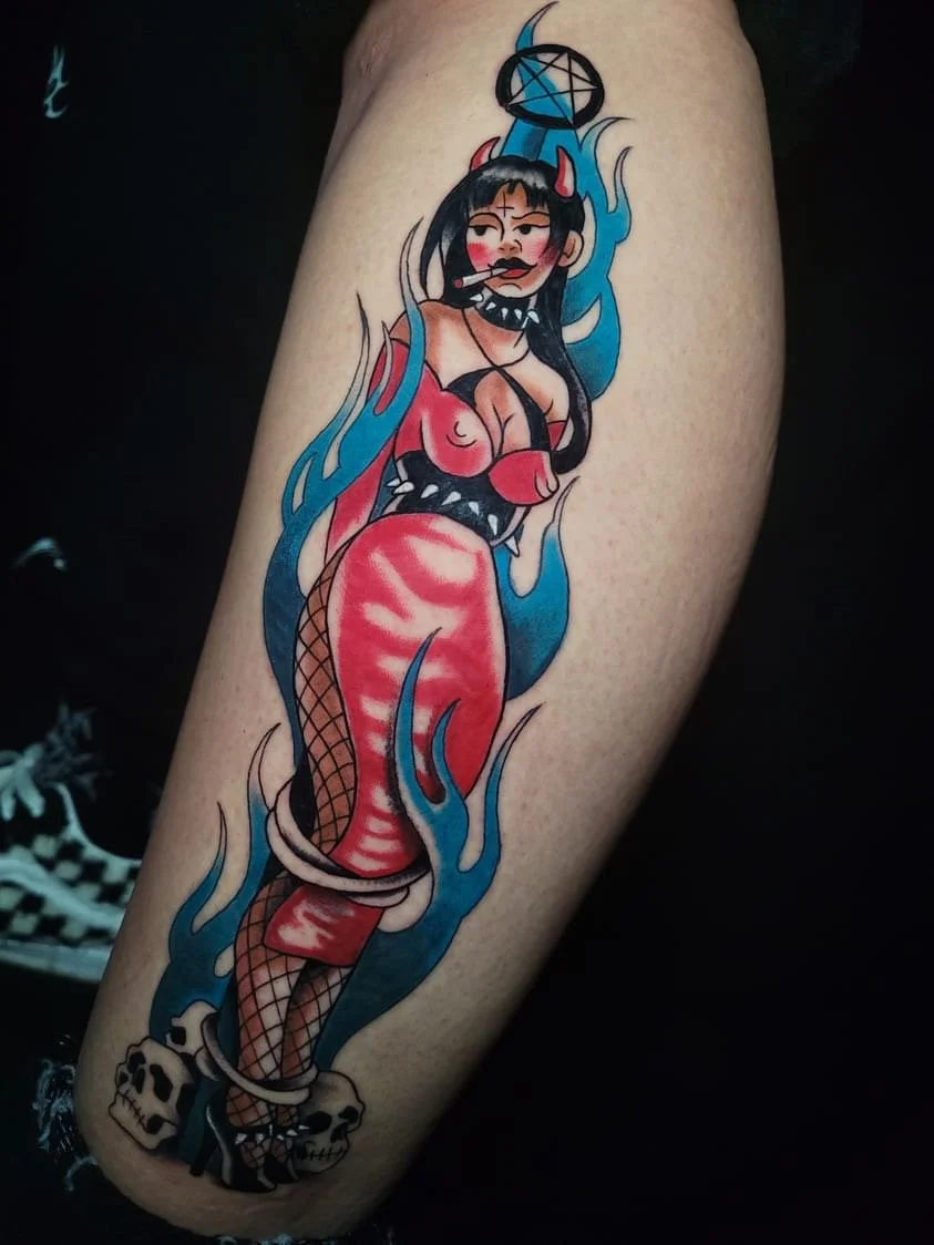A colorful tattoo of a cartoonish woman with horns, devil features, and fishnet stockings, surrounded by flames and skulls, in a provocative pose.