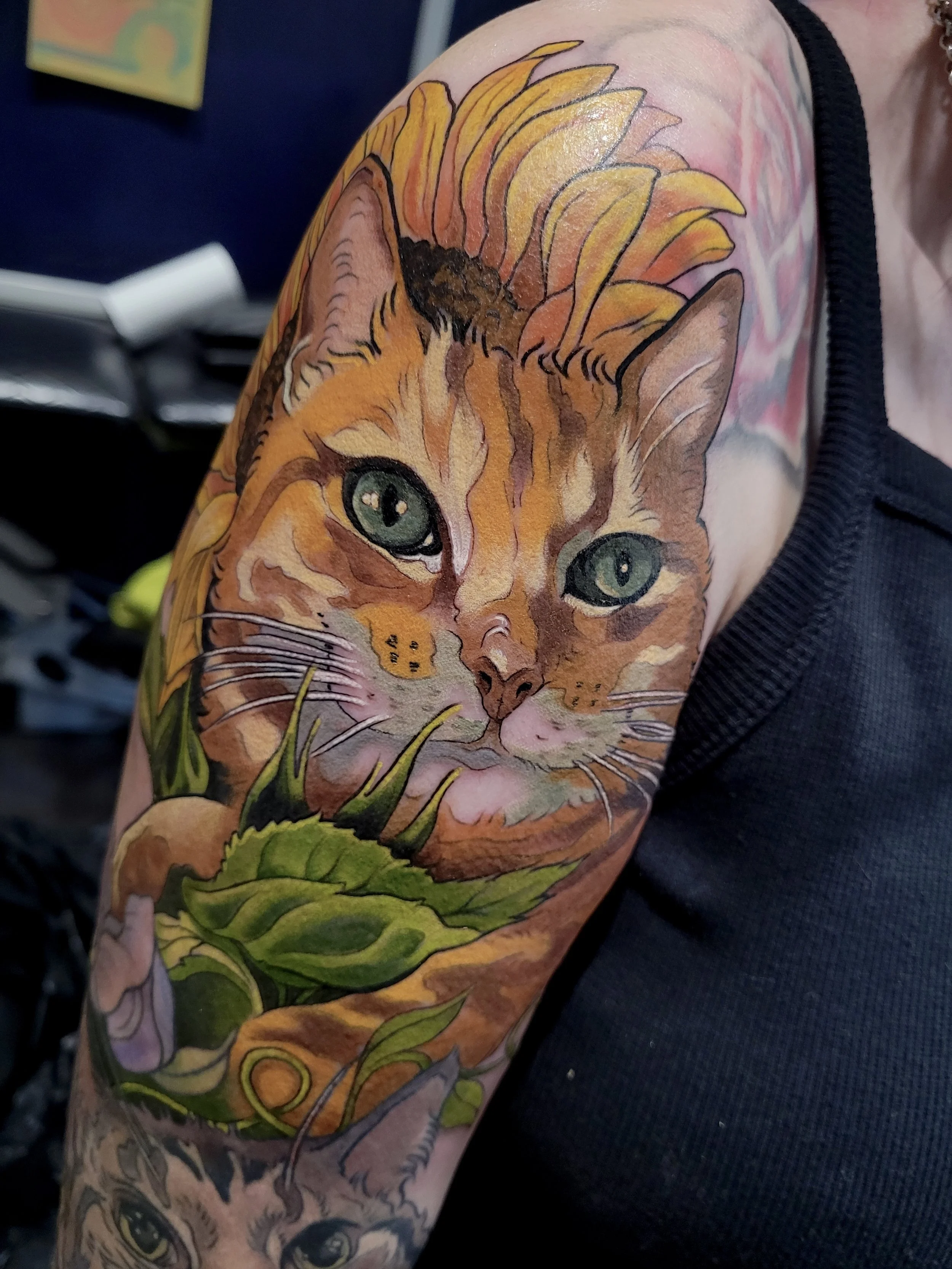 Colorful tattoo of a tiger with green eyes and orange fur, surrounded by green leaves and yellow-orange feathers on a person's upper arm.