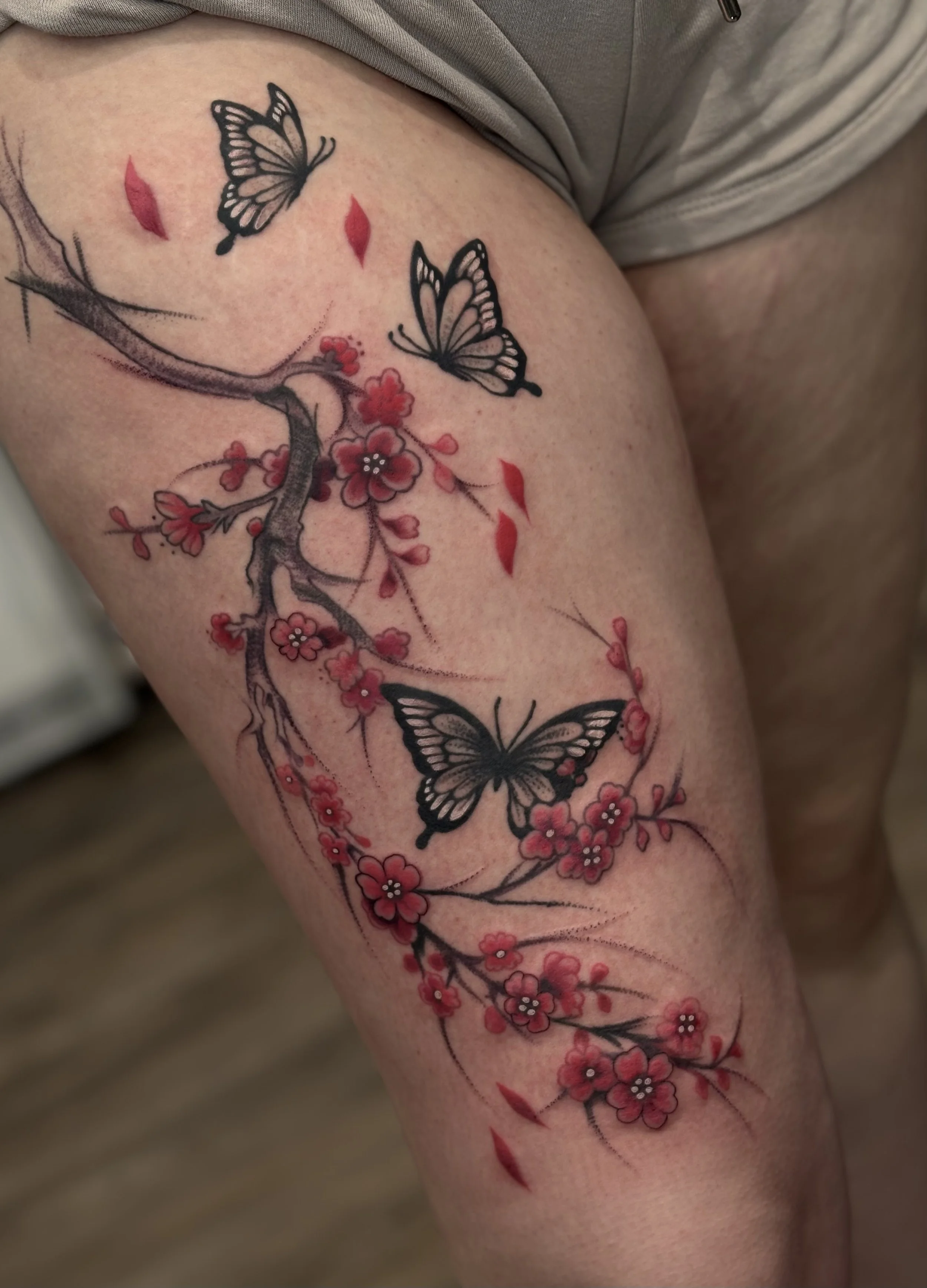 Tattoo of a cherry blossom branch with pink flowers and red petals, featuring two black and white butterflies.