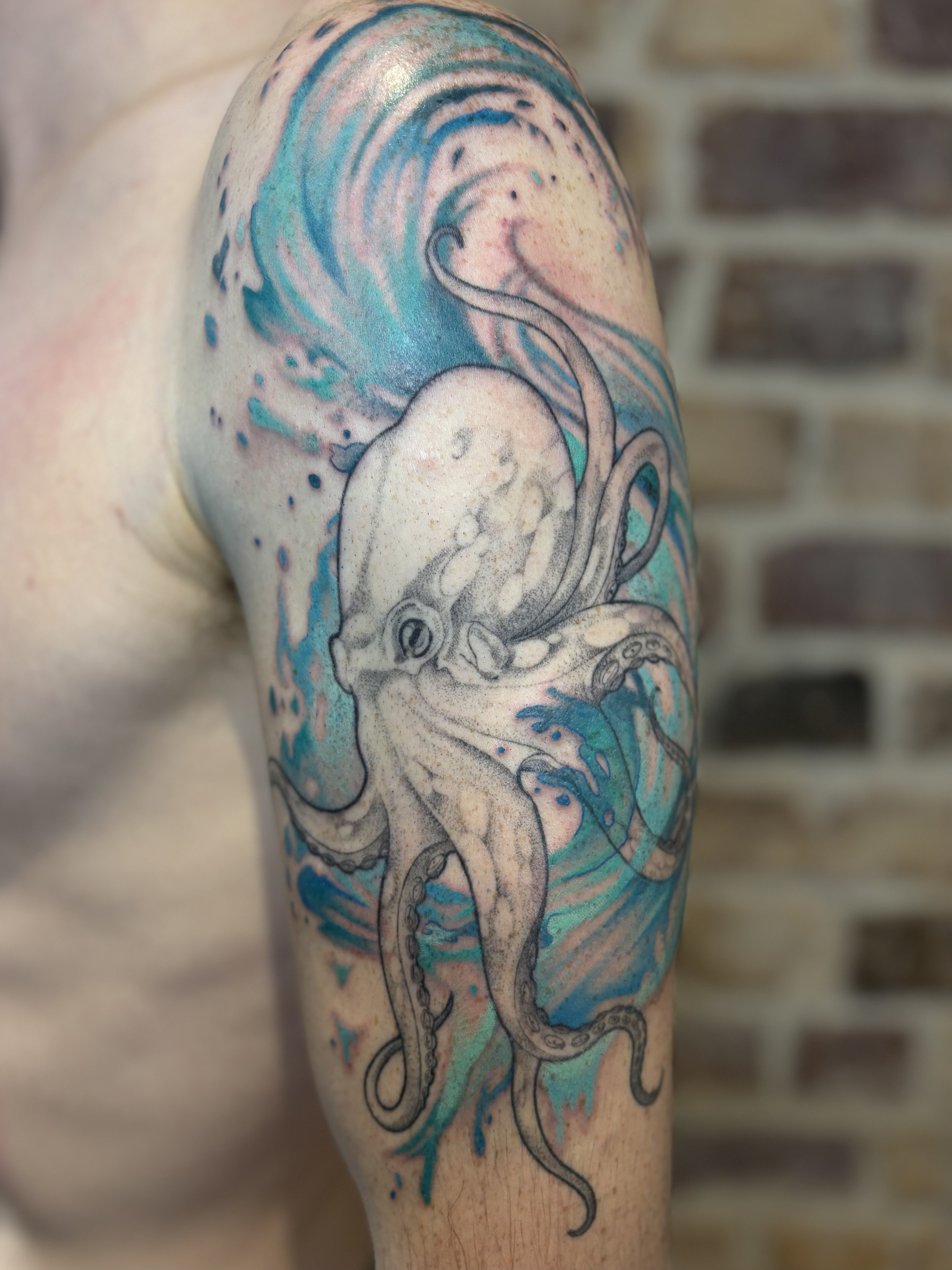 Tattoo of a squid in the ocean with blue water and splash details on a person's upper arm and shoulder.