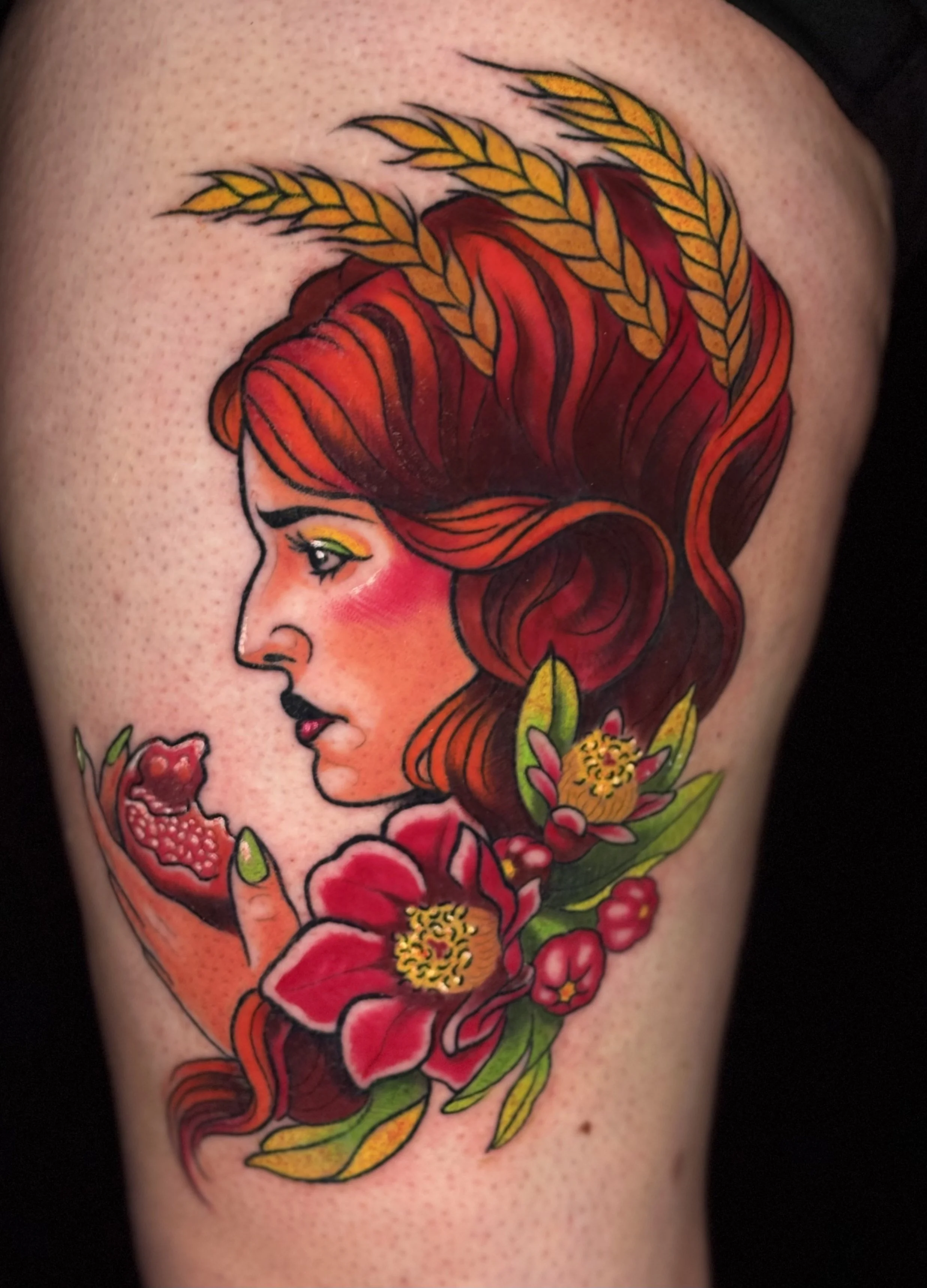 Tattoo of a woman's profile with long, flowing red hair, surrounded by pink flowers, green leaves, and wheat stalks.