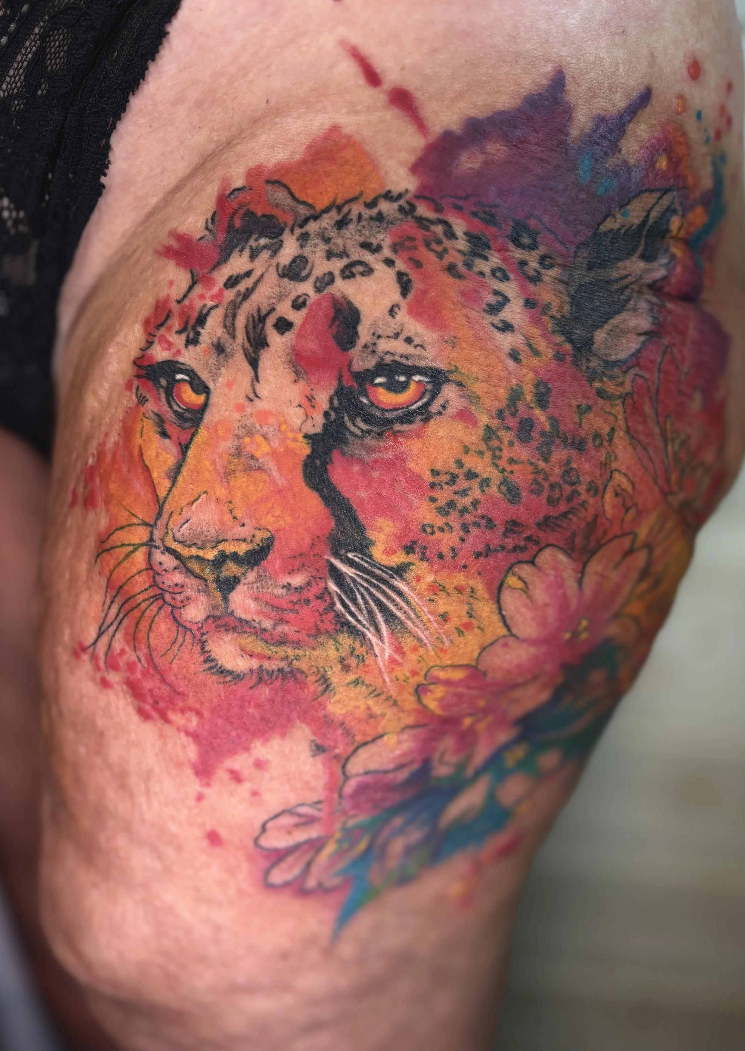 Colorful tattoo of a leopard's face with orange and yellow hues and floral elements on the shoulder.