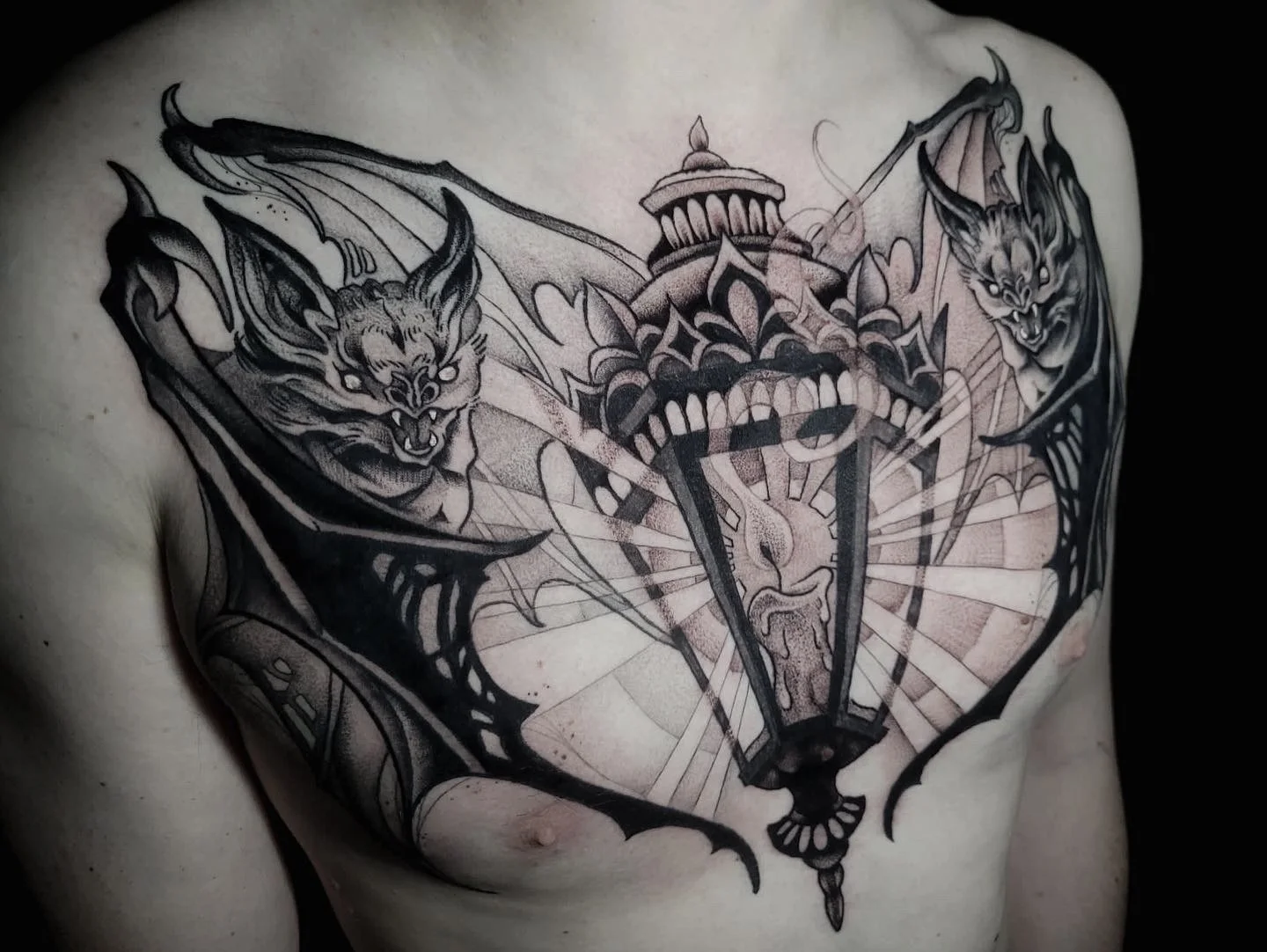 A chest tattoo featuring a broken street lamp with two fierce, winged, snarling cats on either side.