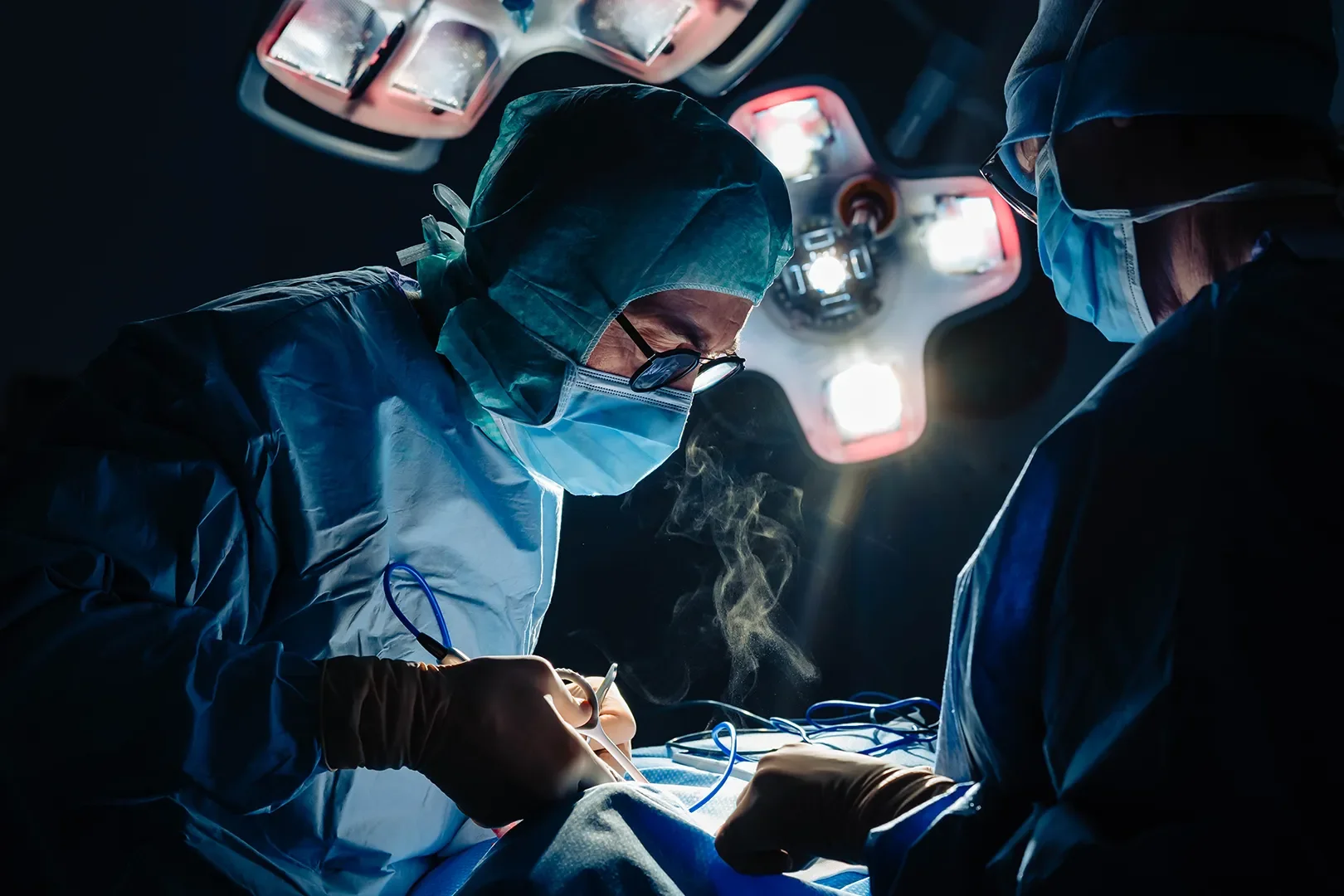 Deux chirurgiens en pleine opération, portant des masques, des gants et des vêtements de protection, travaillant sous une lumière chirurgicale intense dans une salle d'opération.