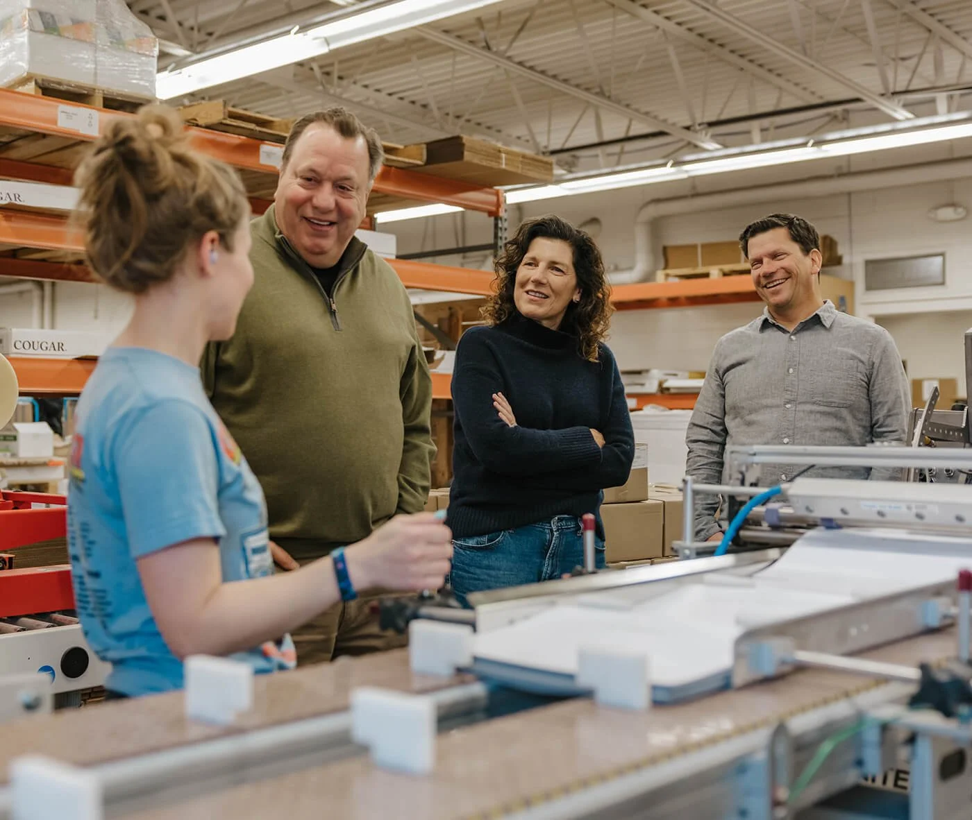 Team members smiling and engaging in conversation with an employee on a shop floor, reflecting a people-first workplace culture.