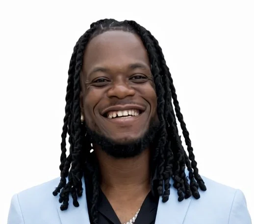 A smiling man with long braided hair wearing a light blue jacket and black shirt.