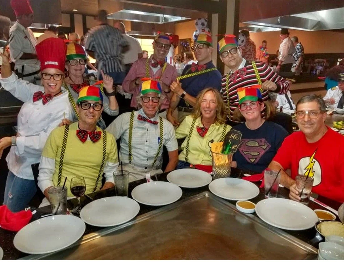 People dressed as clowns and supervillains at a restaurant table with empty plates and drinks.