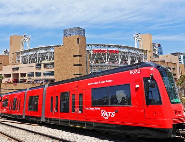 A red Metropolitan Transit System light rail train in front of Petco Park stadium in San Diego, California.