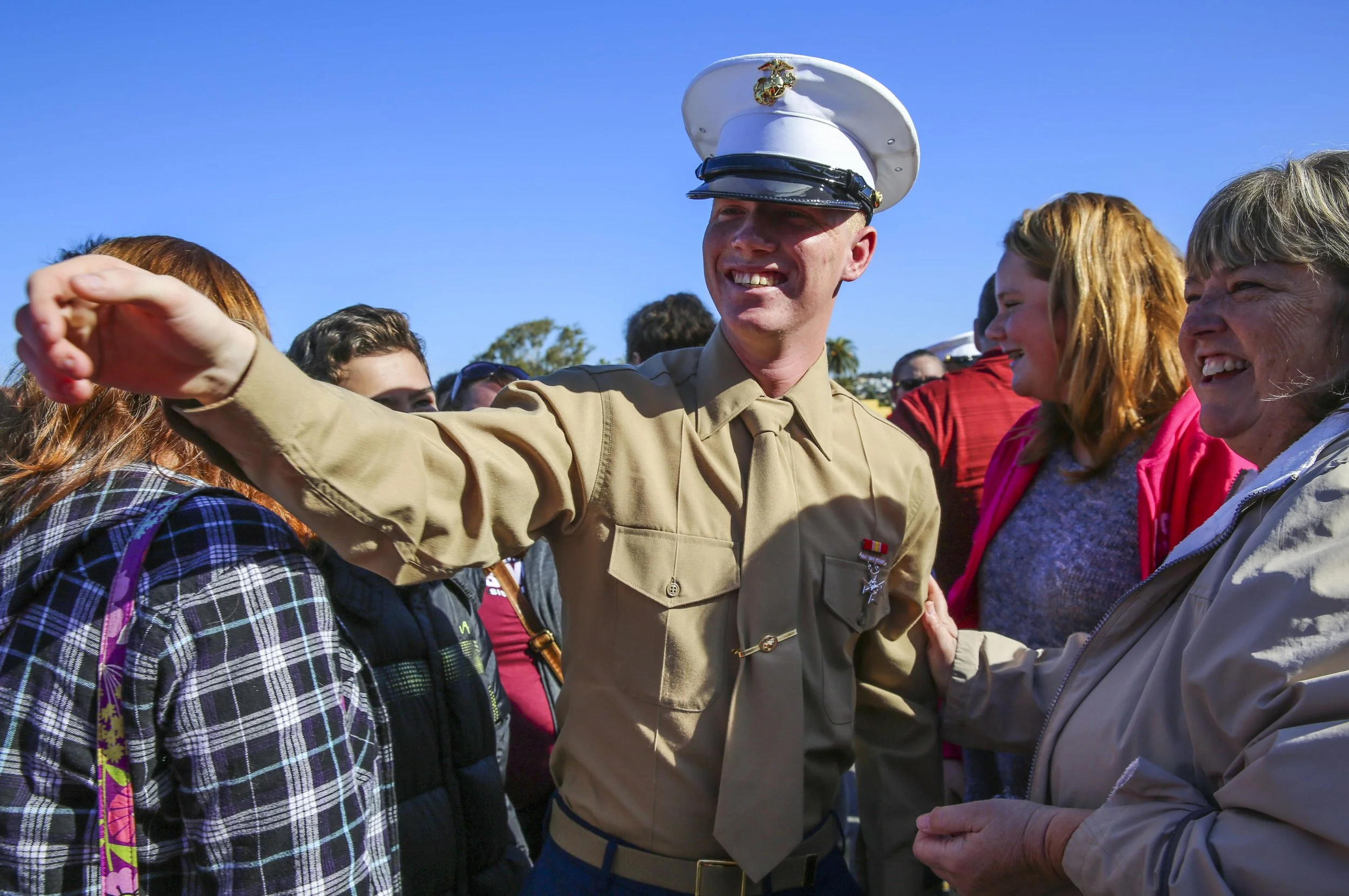 U.S. Marine in dress uniform smiling and interacting with a group of women outdoors on a sunny day