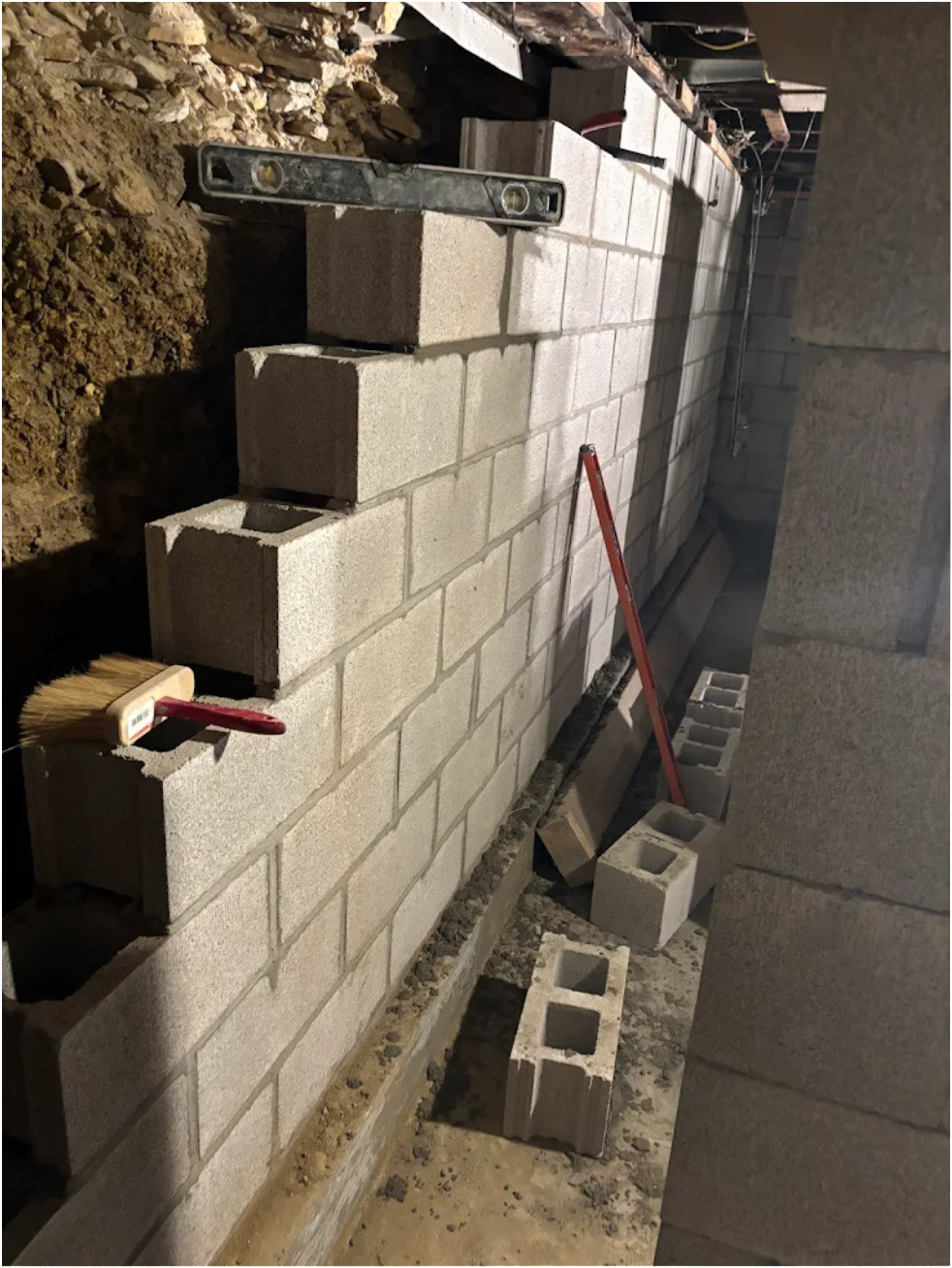 Construction site showing cinder block wall being built, with construction tools and supplies like a level, broom, and mortar on top of the blocks.