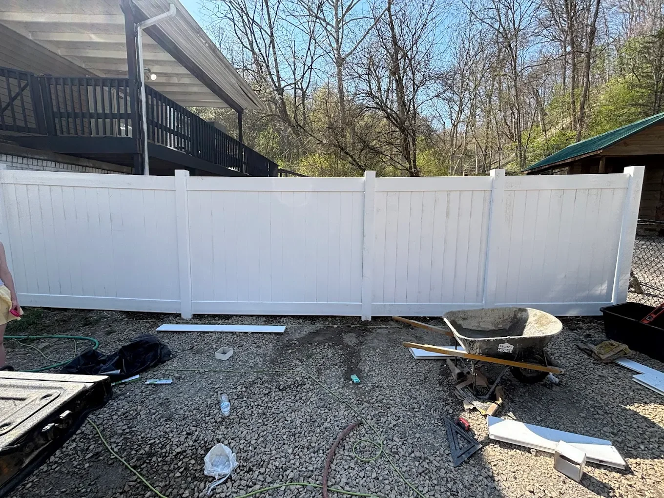 Completed white privacy fence in a backyard with construction tools and debris on the ground.