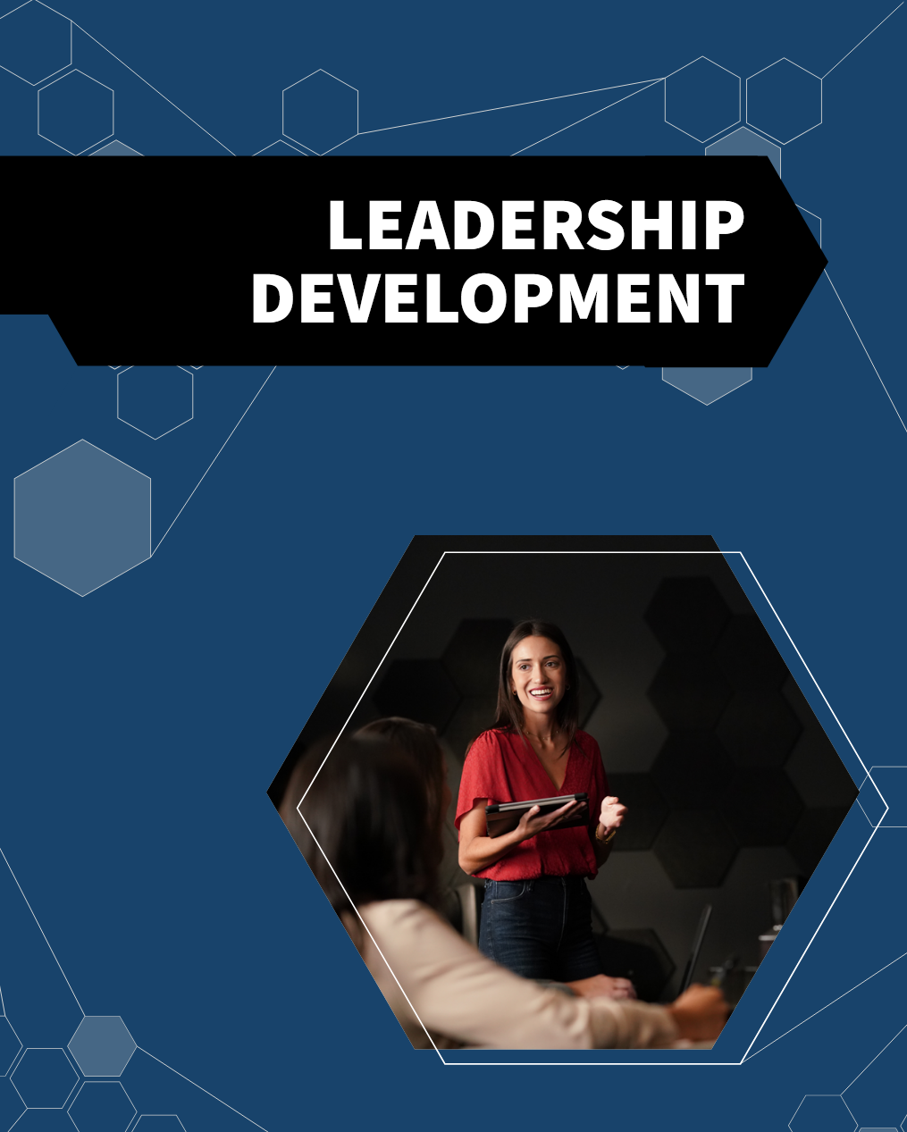 A woman giving a presentation or leading a discussion in a professional setting, with a laptop on the table and other participants listening.