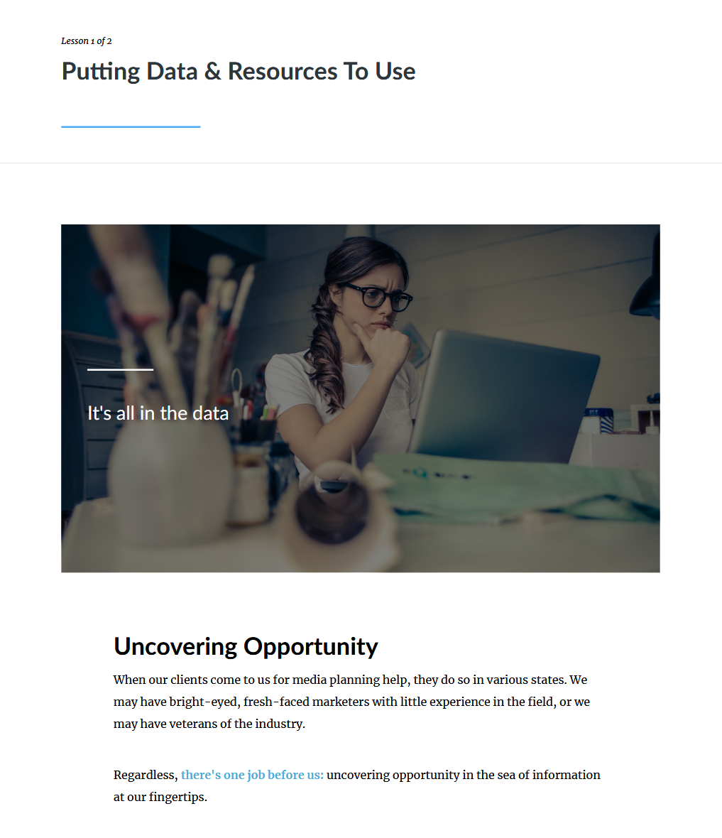 A woman with glasses sitting at a desk with a laptop, looking thoughtful while working, in a well-lit room.