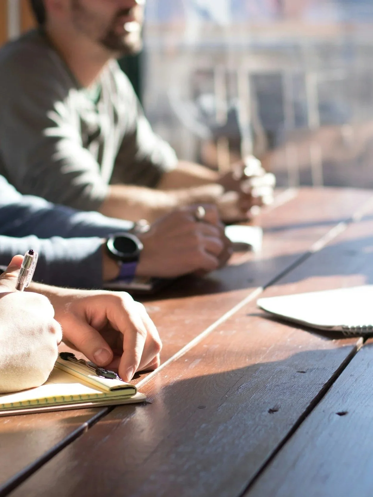 image of people having a conversation at a sunlit table with notebooks