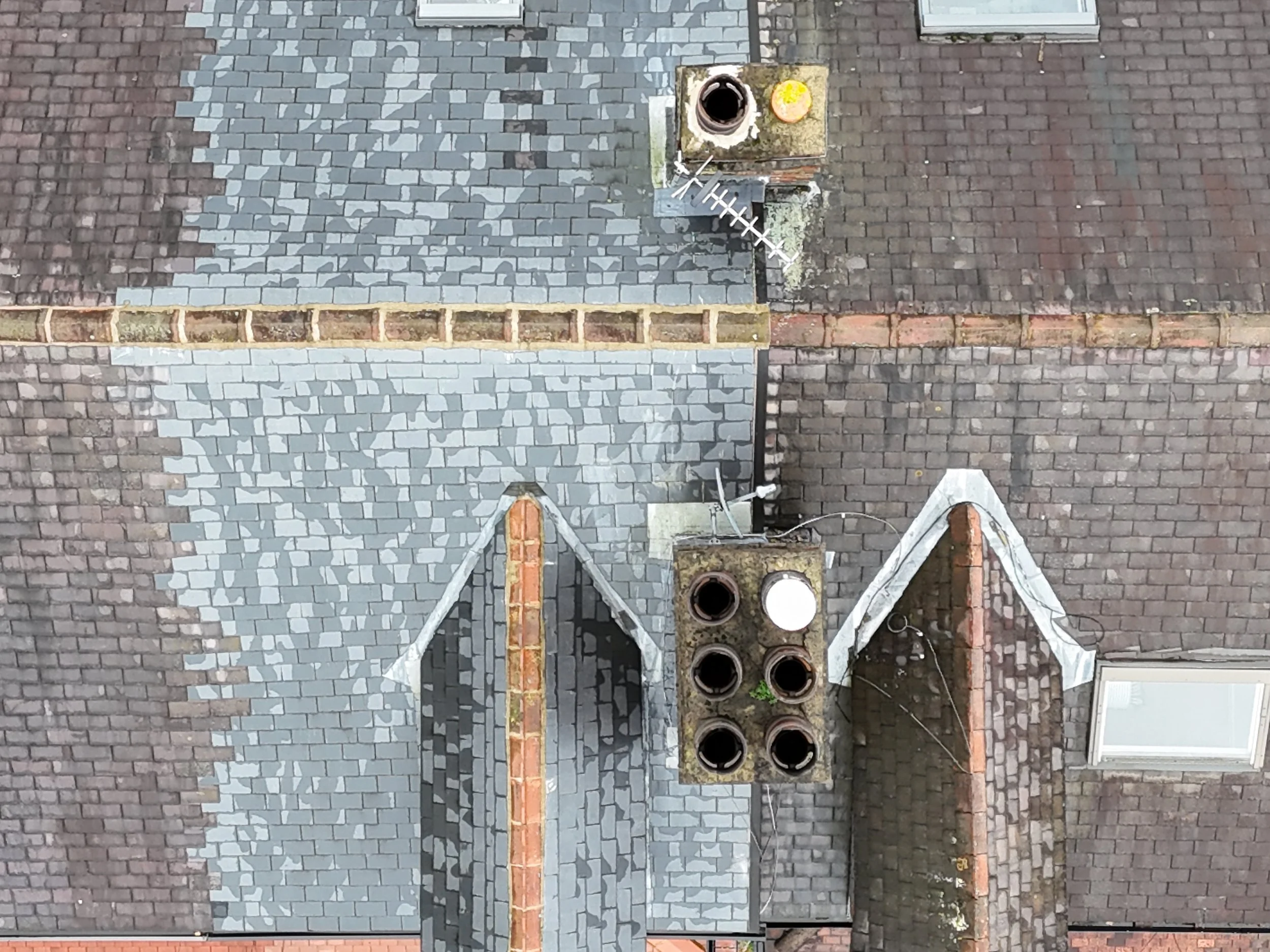 A rooftop with construction work in progress, showing partially completed gray and red brick roofing, a row of round vents, and some construction tools. The rooftop includes sections with different types of brickwork and materials.