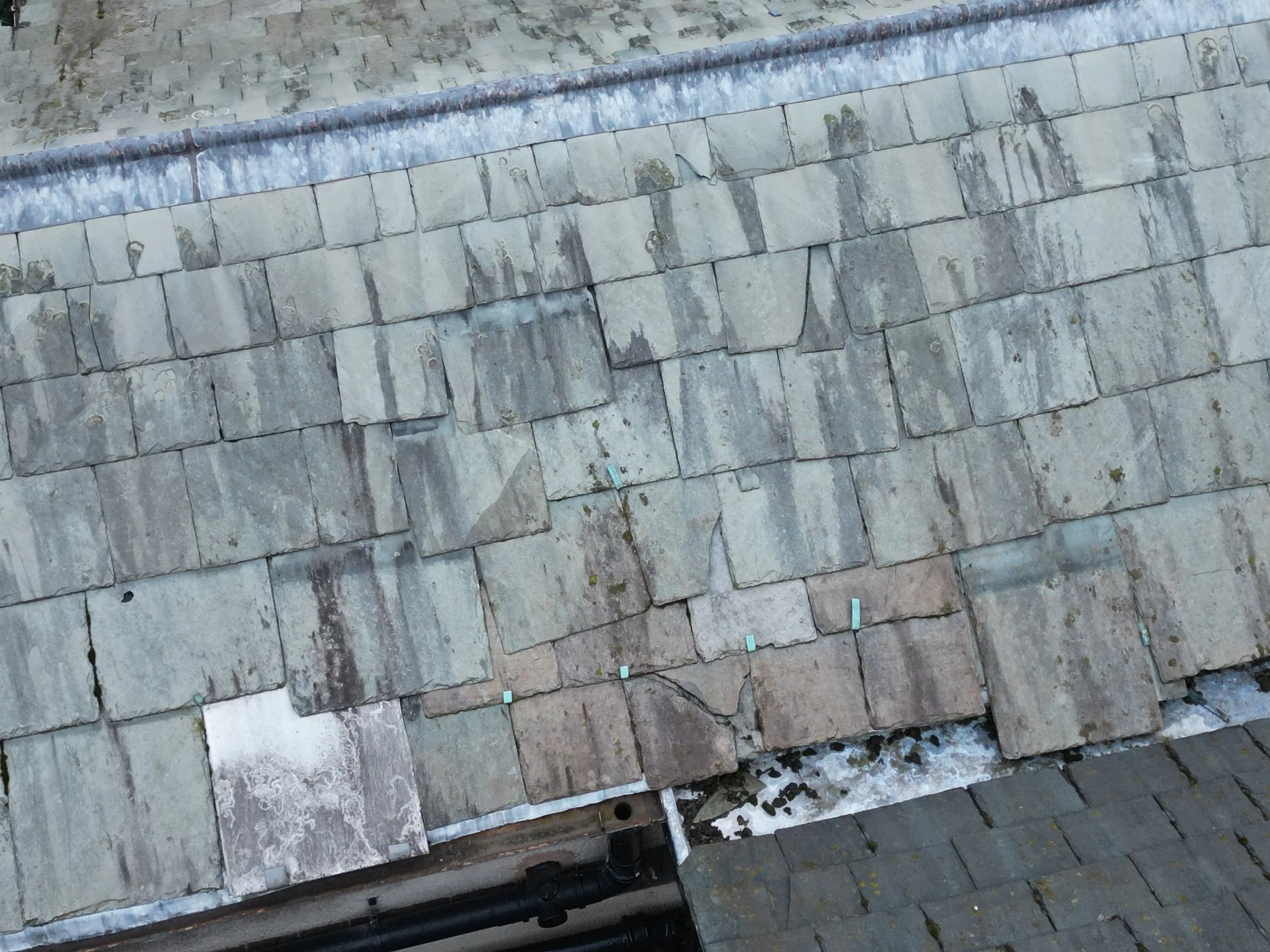 Close-up of a roof with layered gray slate tiles and black drainage pipes installed at the bottom.