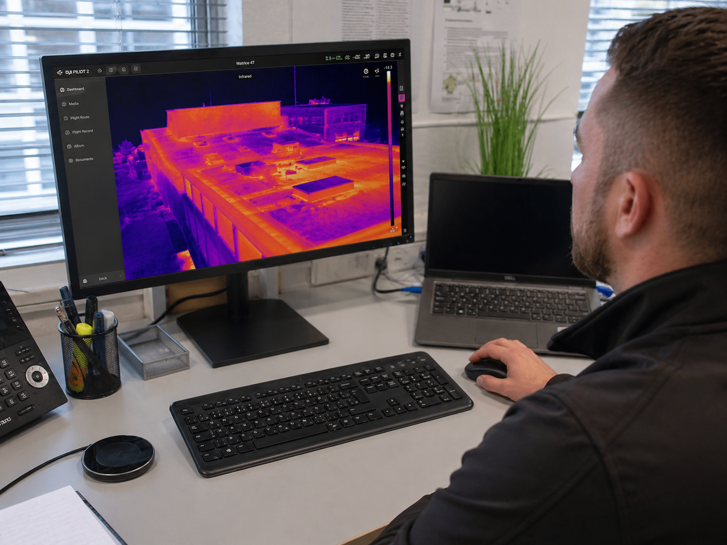 Man at desk analyzing a thermal image of a building on a computer monitor.