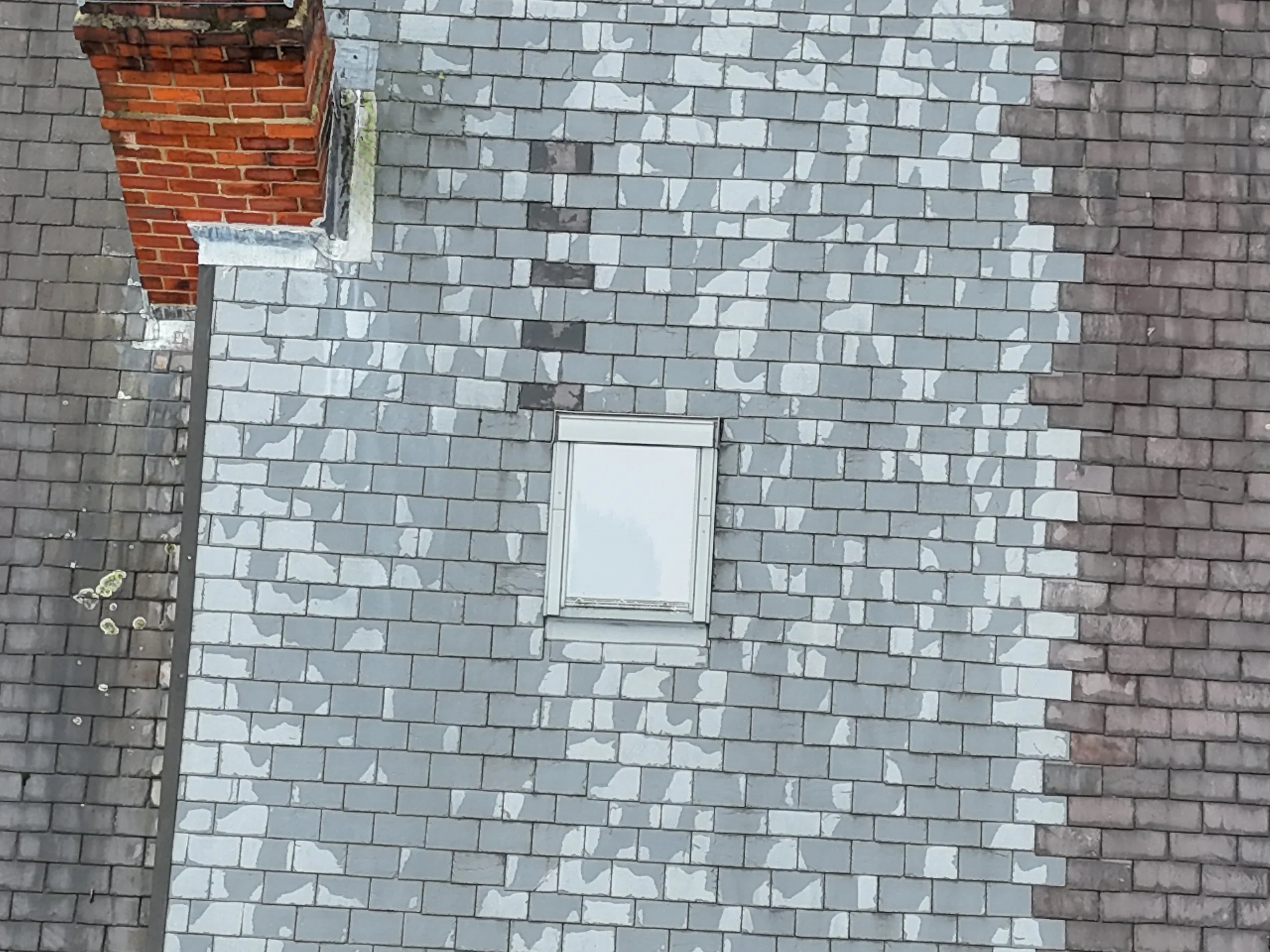 A building's exterior wall made of brick and stone, with a small window and a chimney on the roof.