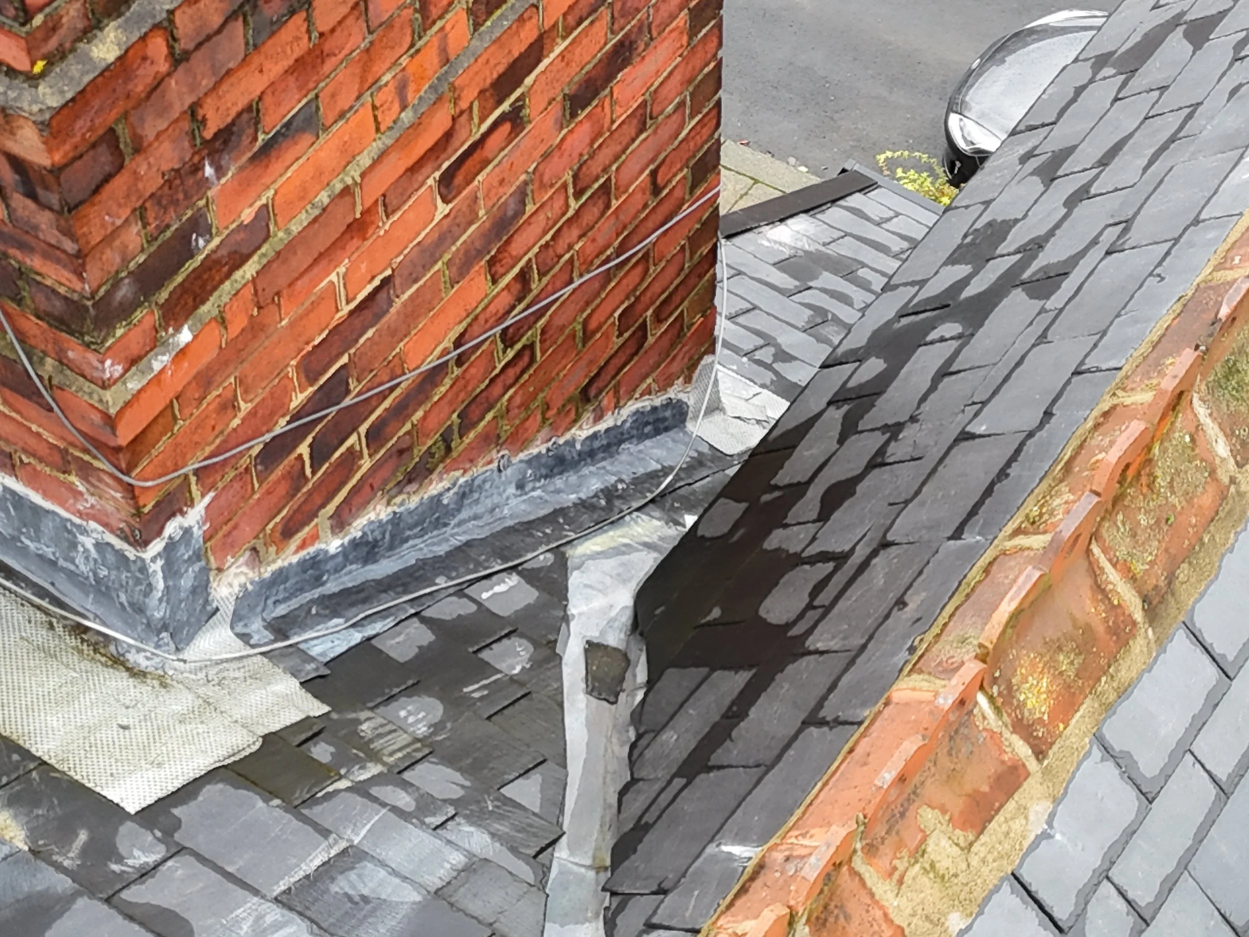 Close-up image of a red brick chimney and a gray shingled roof.
