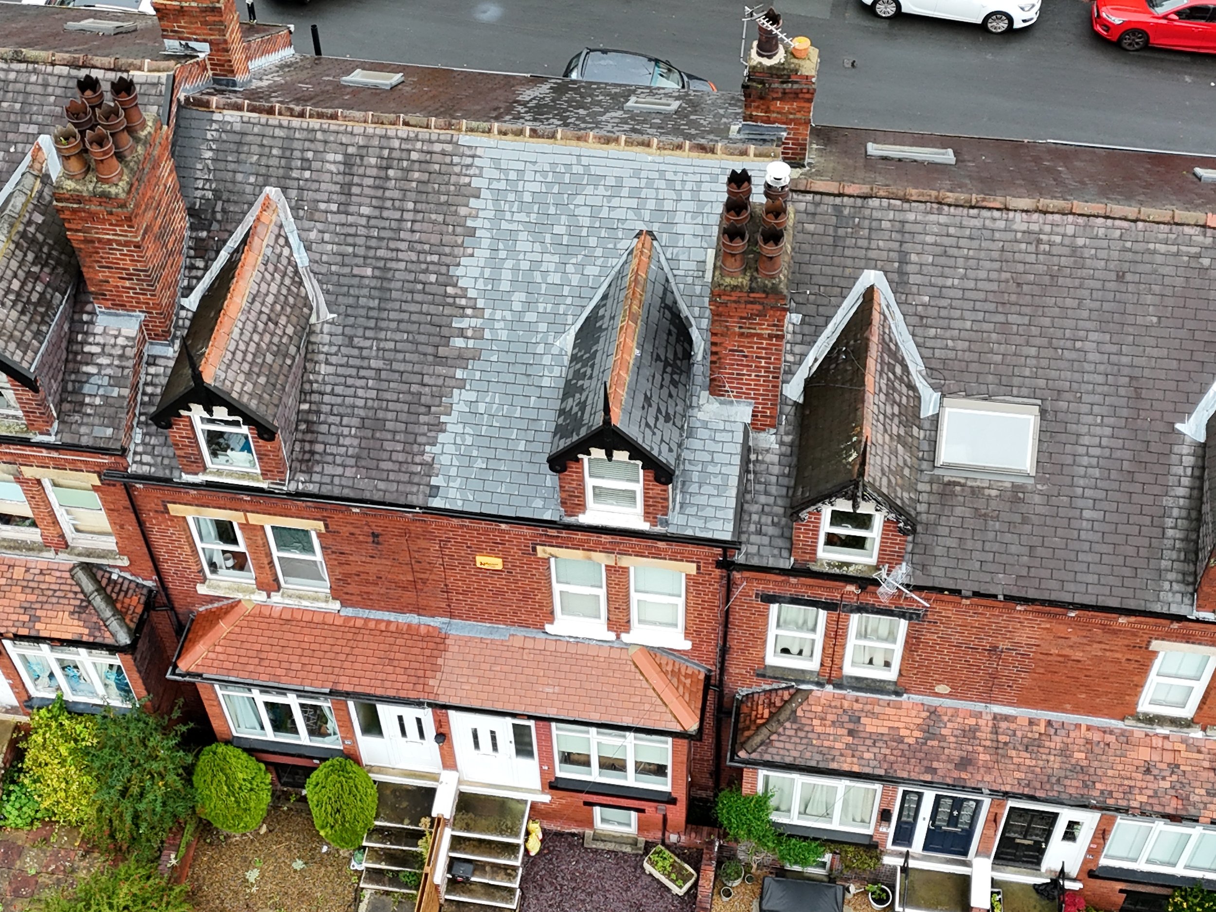 Aerial view of a row of brick houses with peaked roofs, chimneys, and windows, along with a parking area and some greenery in the yard.