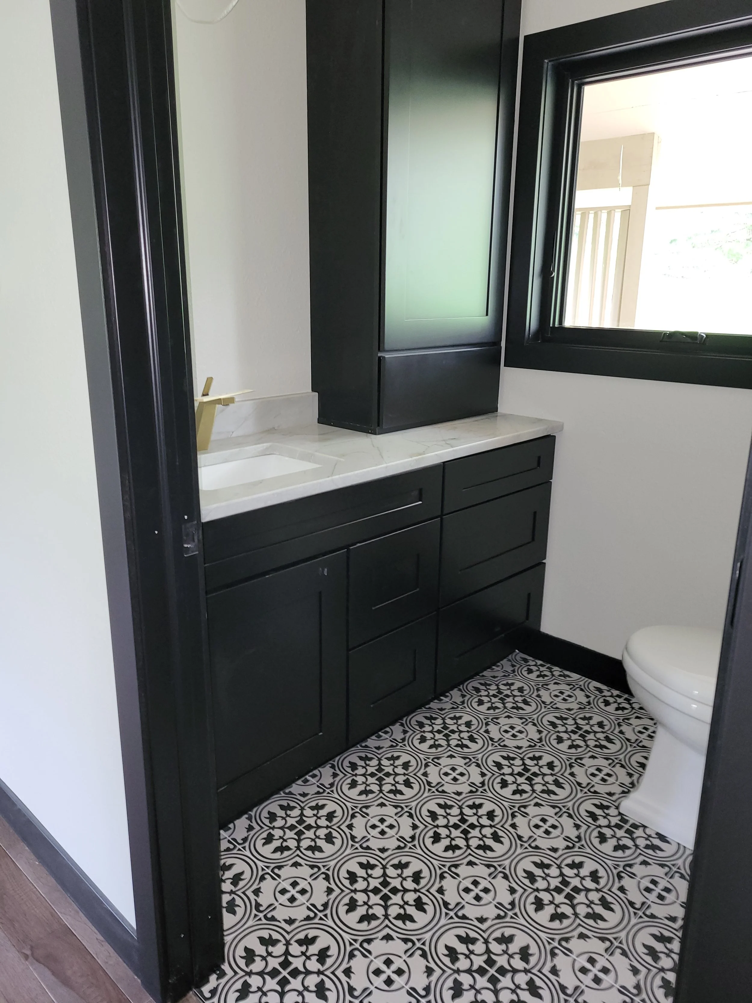 A modern bathroom with black cabinets, a white quartz countertop, new tile floor and new casement window.