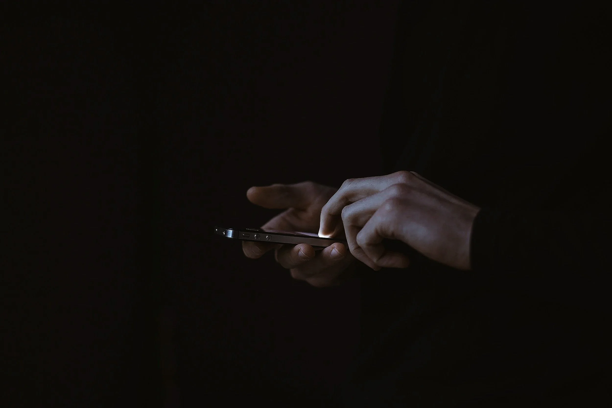 Person using a smartphone in a dark environment, with the screen providing illumination.
