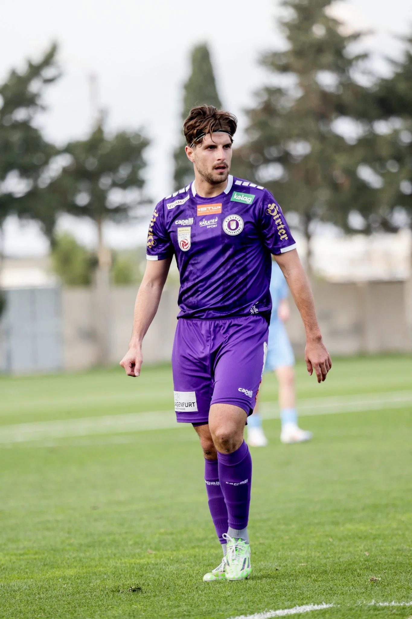 Ein junger Mann trägt ein lila Fußballtrikot und -shorts, steht auf einem Fußballfeld, während er sich anscheinend auf das Spiel konzentriert.